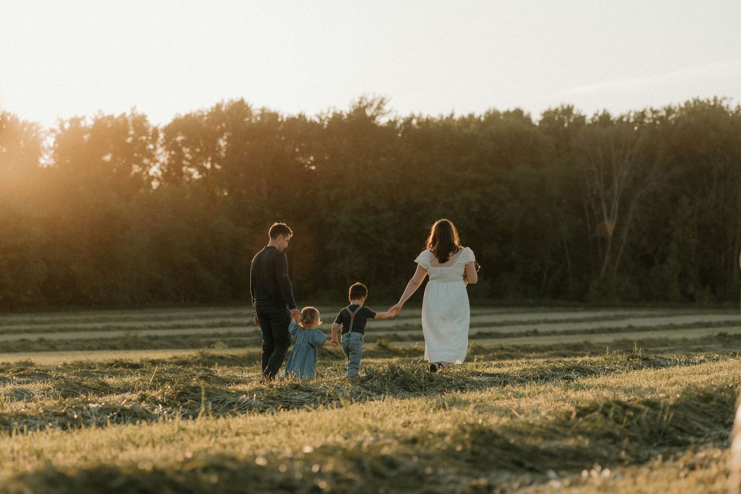 Family walking together in sunlit field during golden hour.