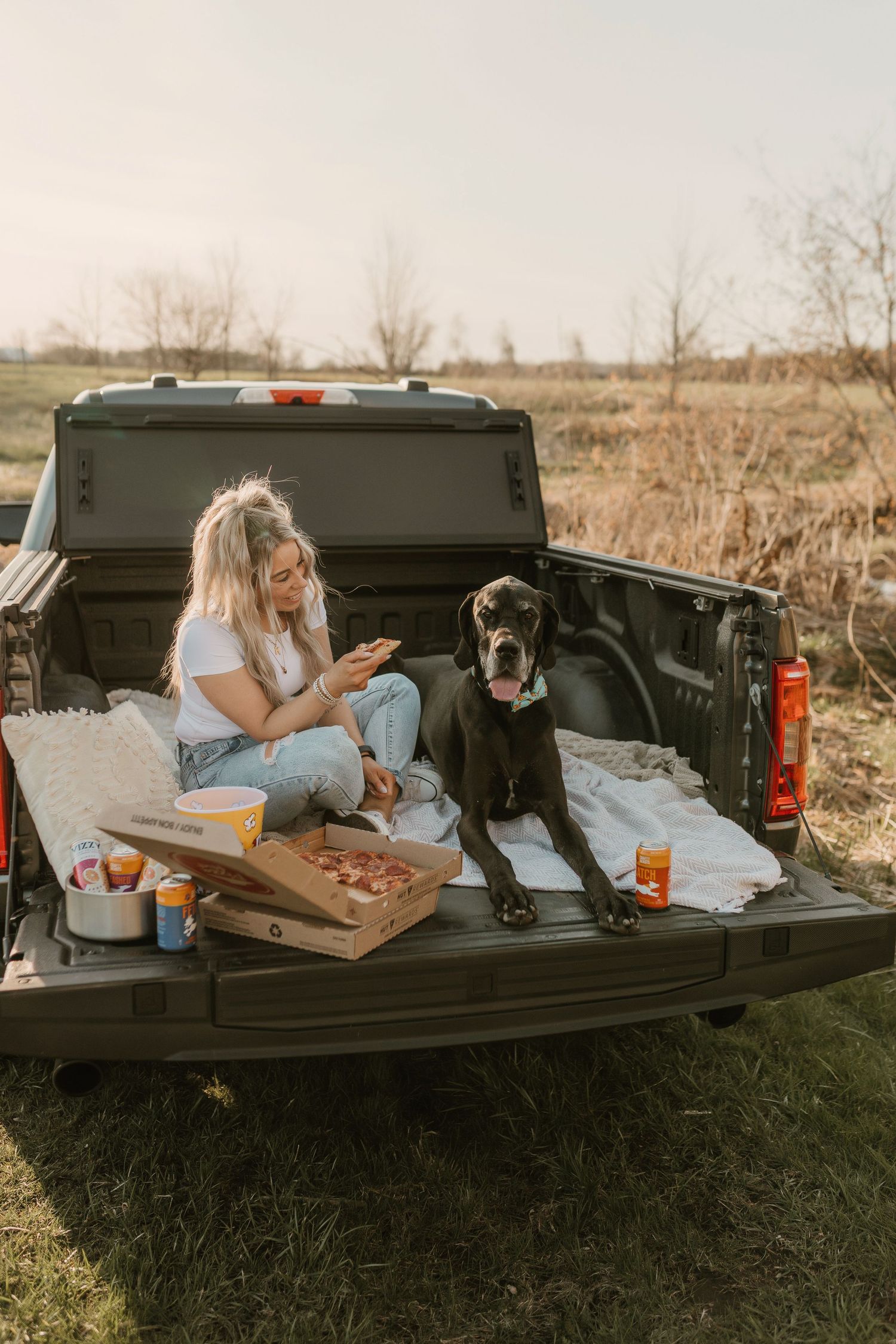 Pizza and drinks in pickup truck bed during sunset in rural setting.