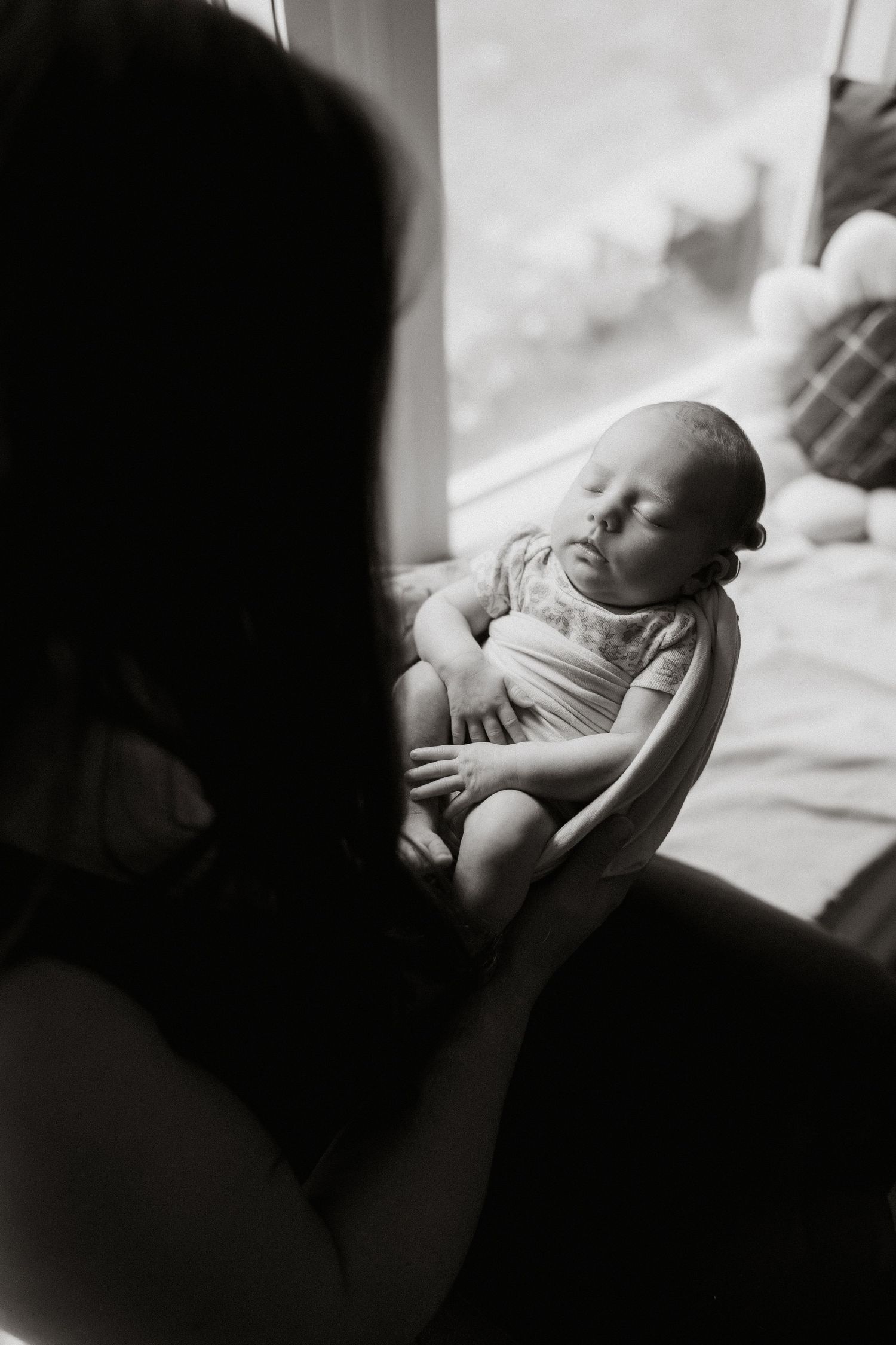 Black and white artistic series of photos showing a newborn baby sleeping peacefully on soft bedding.