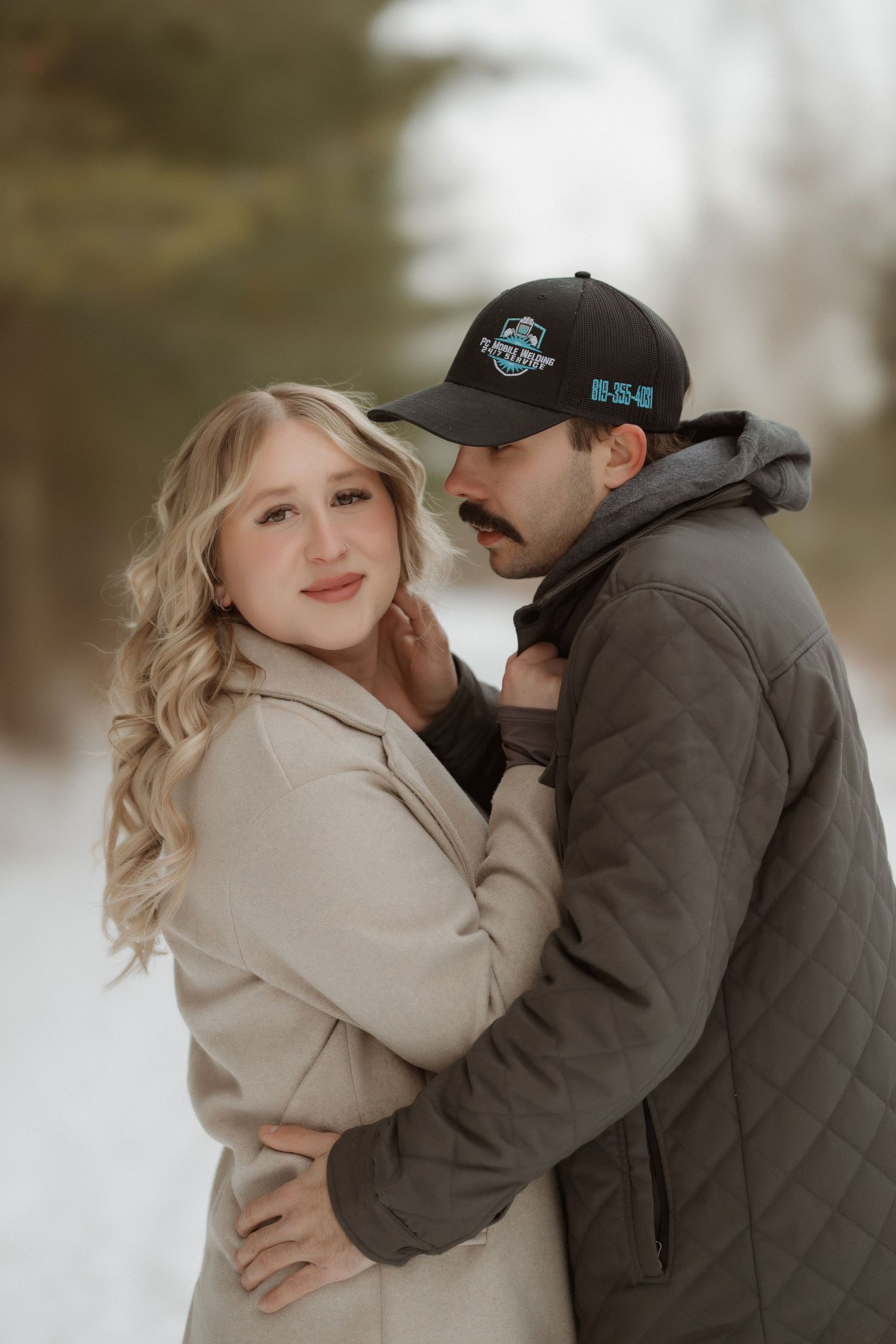 A winter engagement photo of a couple embracing in the snow.