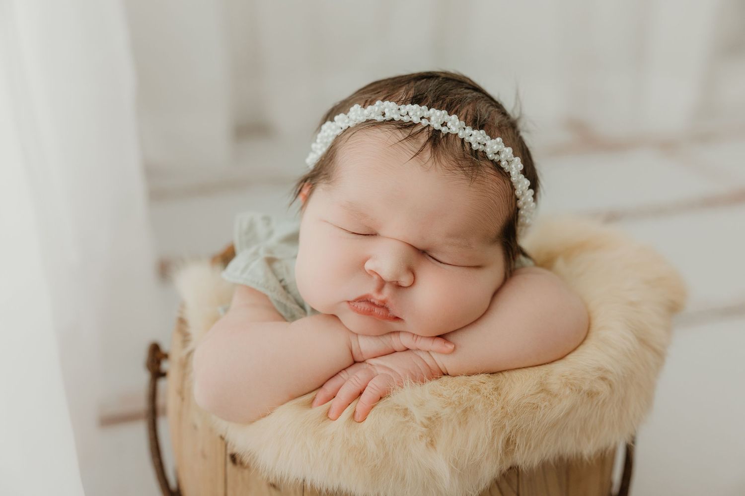 Newborn baby sleeping peacefully on cream-colored fur with delicate headband.