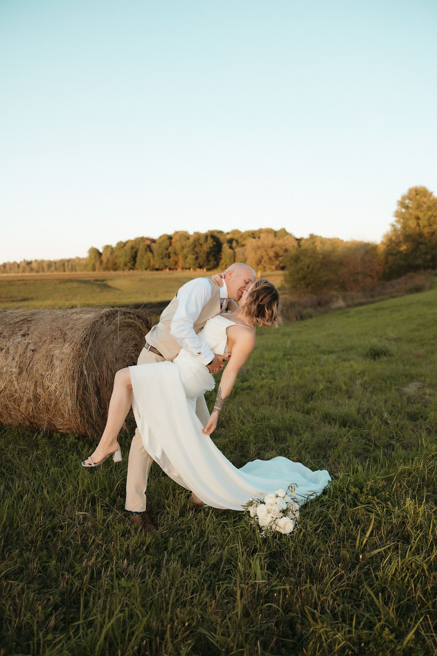 Person in white dress laying in grassy field during golden hour with flowers.