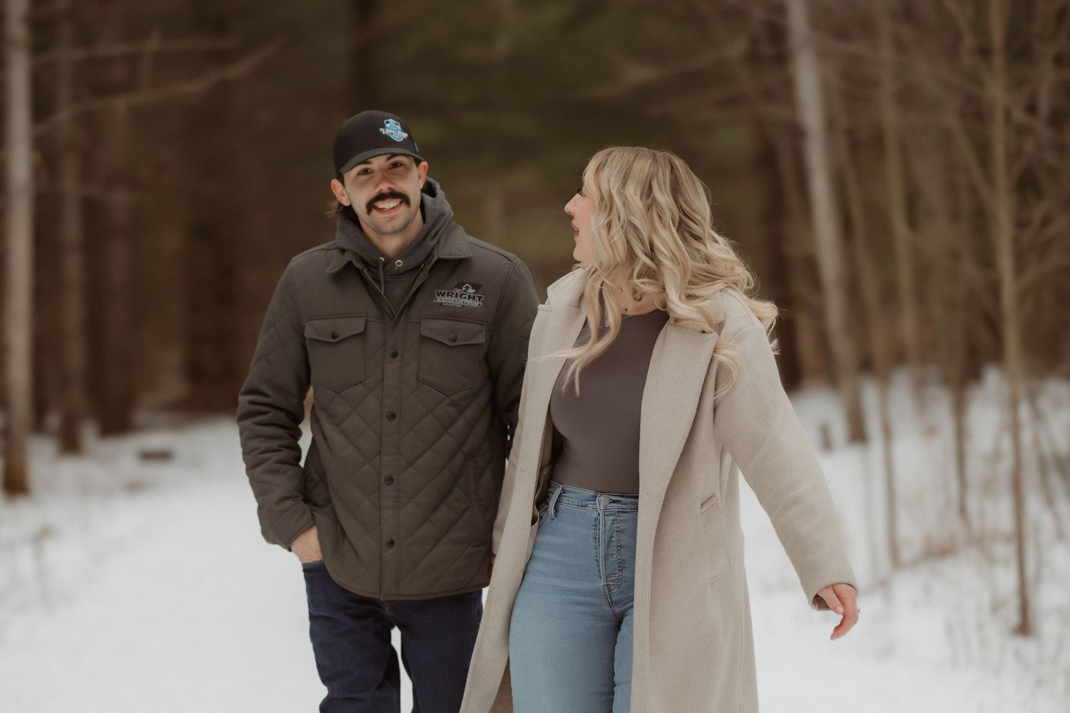 A couple shares a happy moment while walking through a snowy forest path.