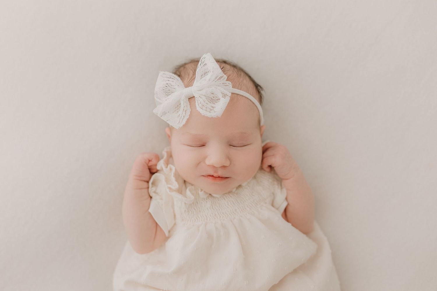 Sweet newborn photos with white lace dress and bow headband on soft backdrop.