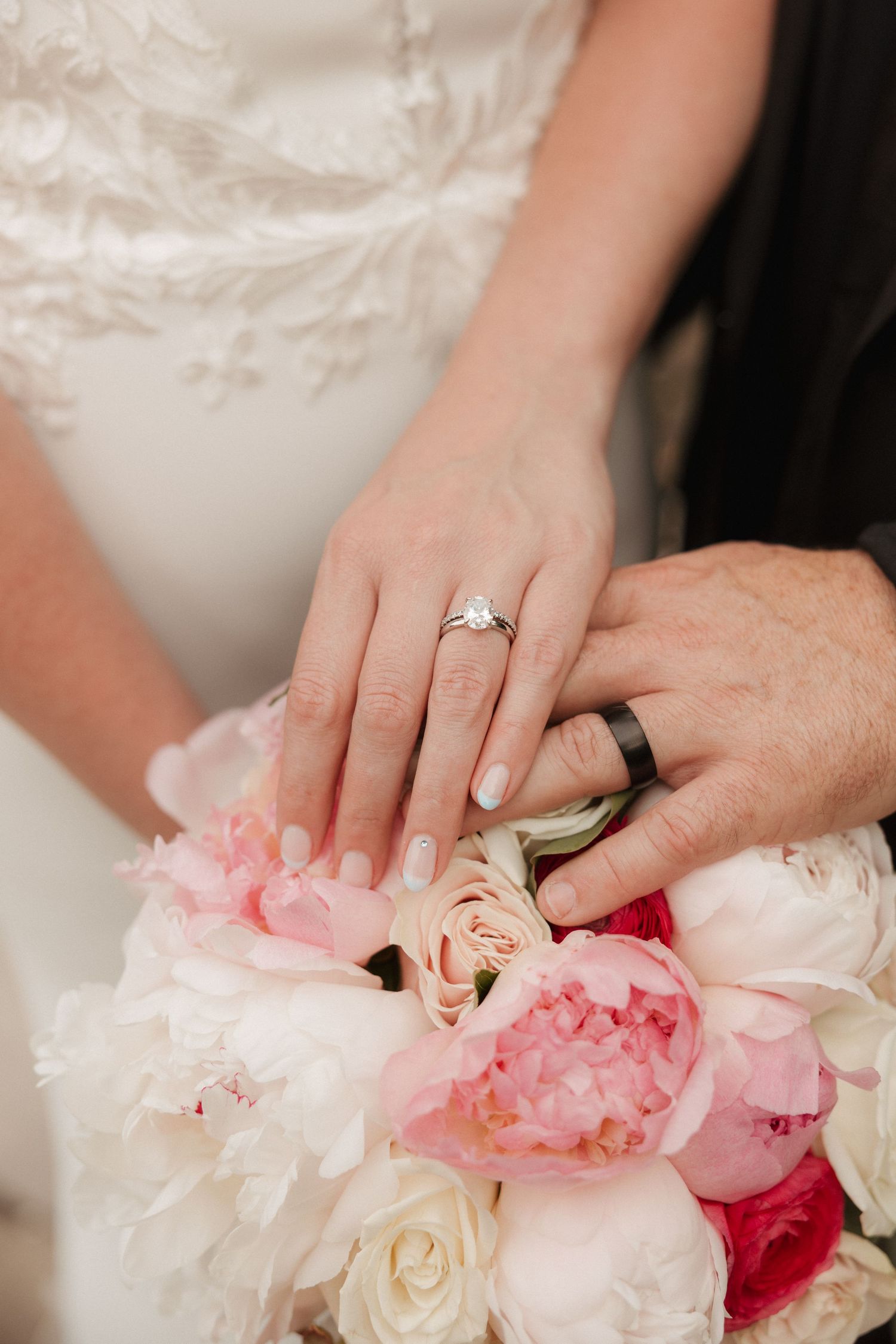 Wedding rings are showcased against a bouquet of pink and white roses and peonies.