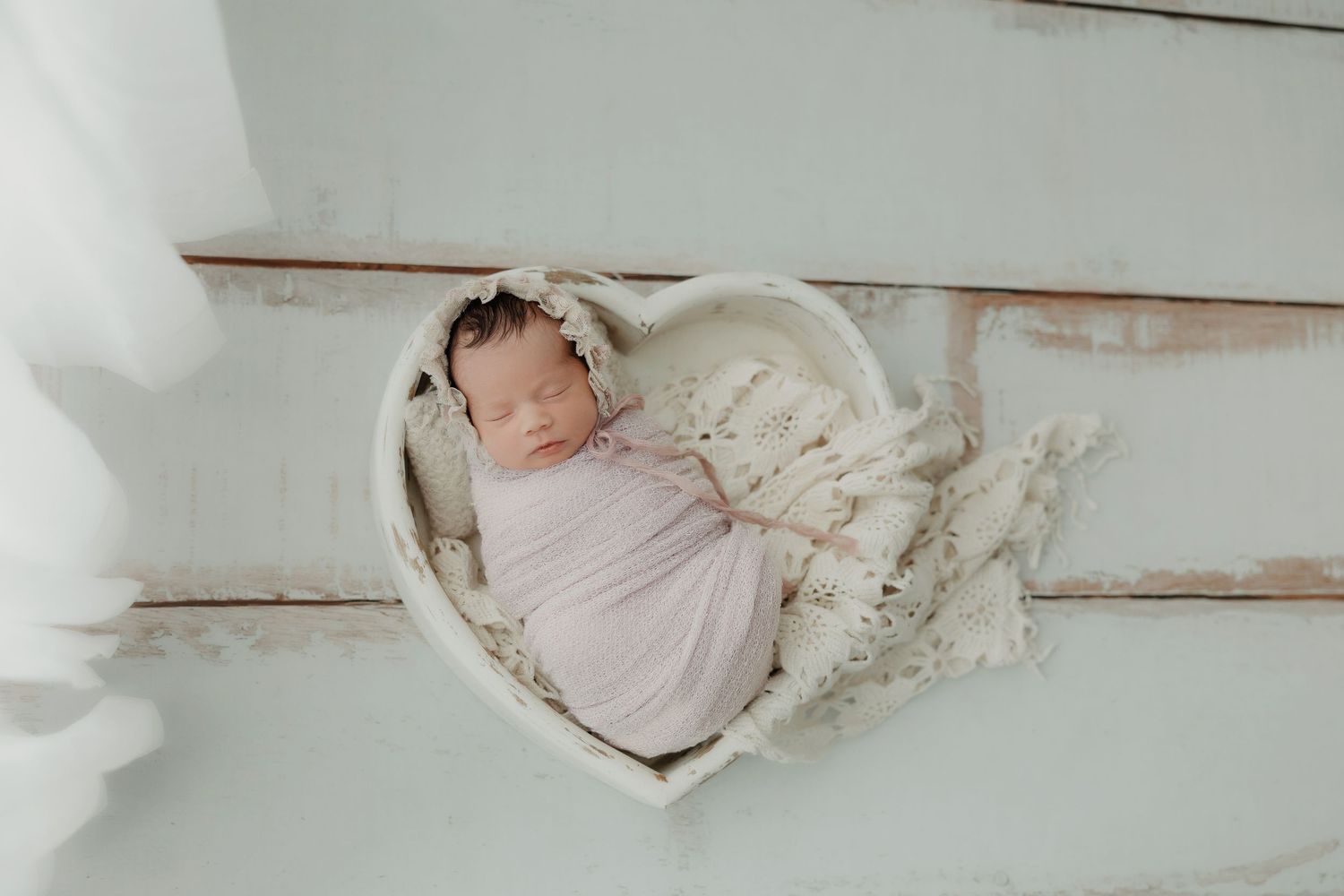 Sleeping newborn baby wrapped in soft pink fabric lying in a heart-shaped prop.