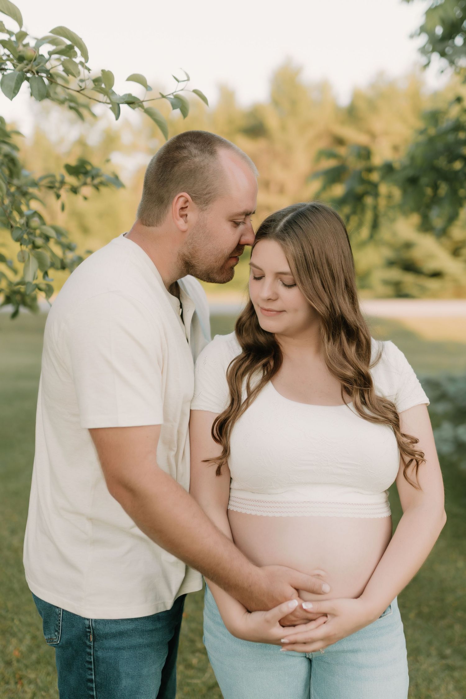 An intimate outdoor maternity photo of a couple embracing in a garden setting.