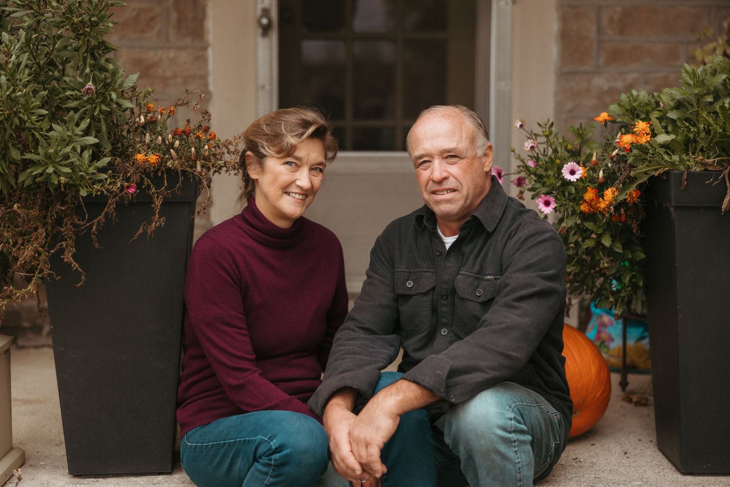 A fall-themed portrait on a porch with potted mums and pumpkins.