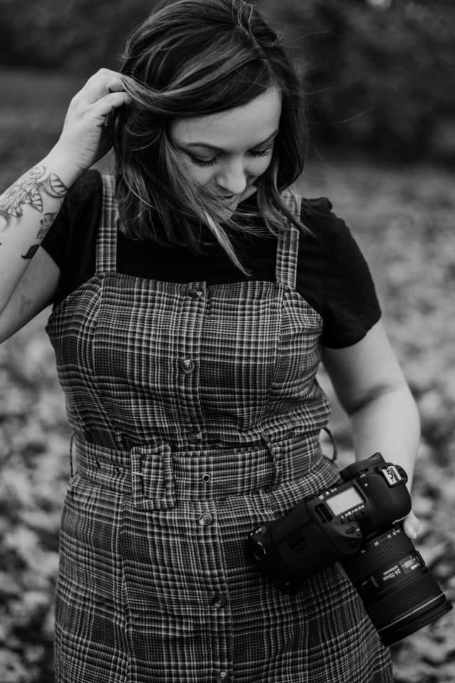 Photographer wearing plaid overalls and black shirt holding a camera in monochrome style.