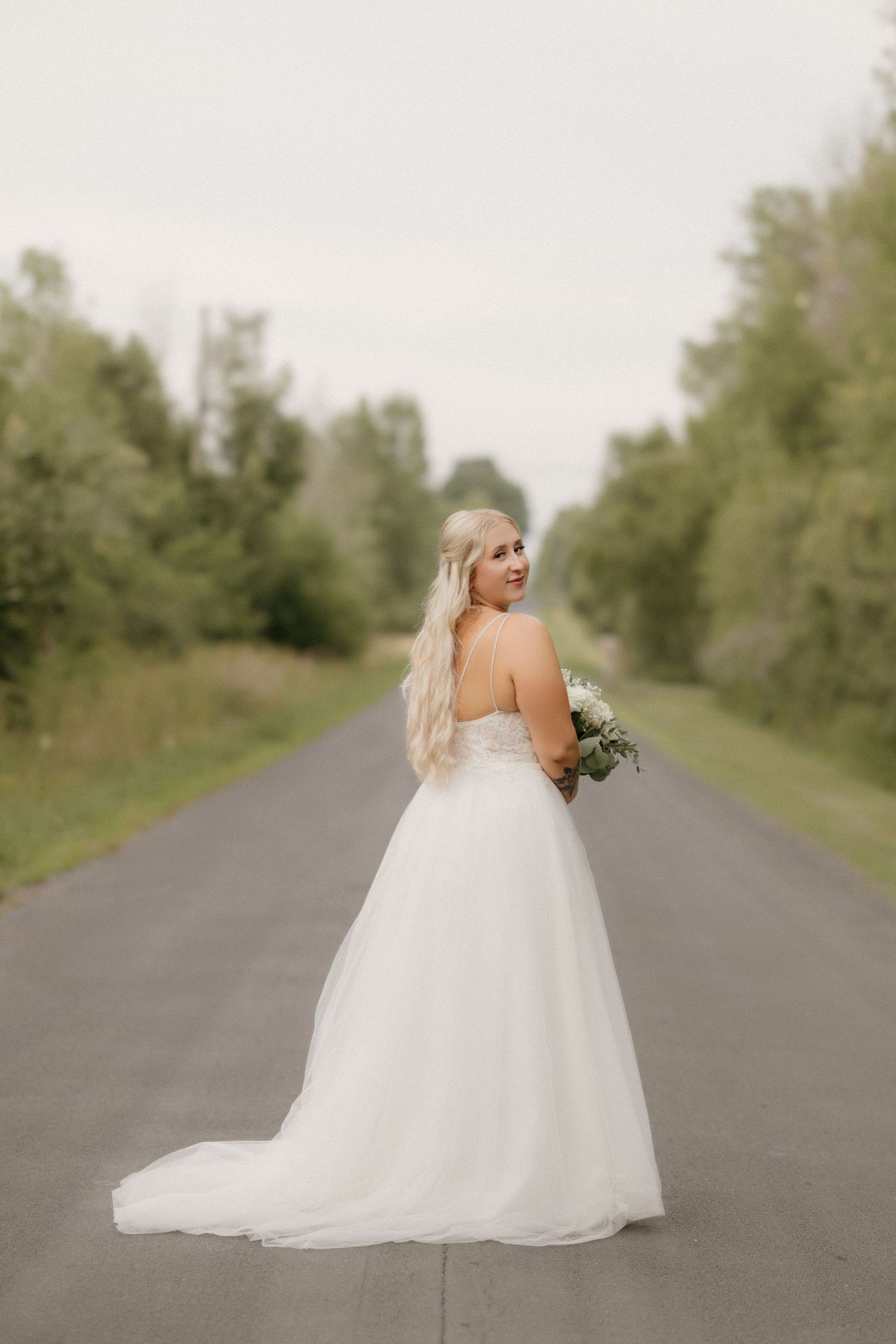 Bride in flowing white ballgown poses on empty road during sunset wedding photoshoot.