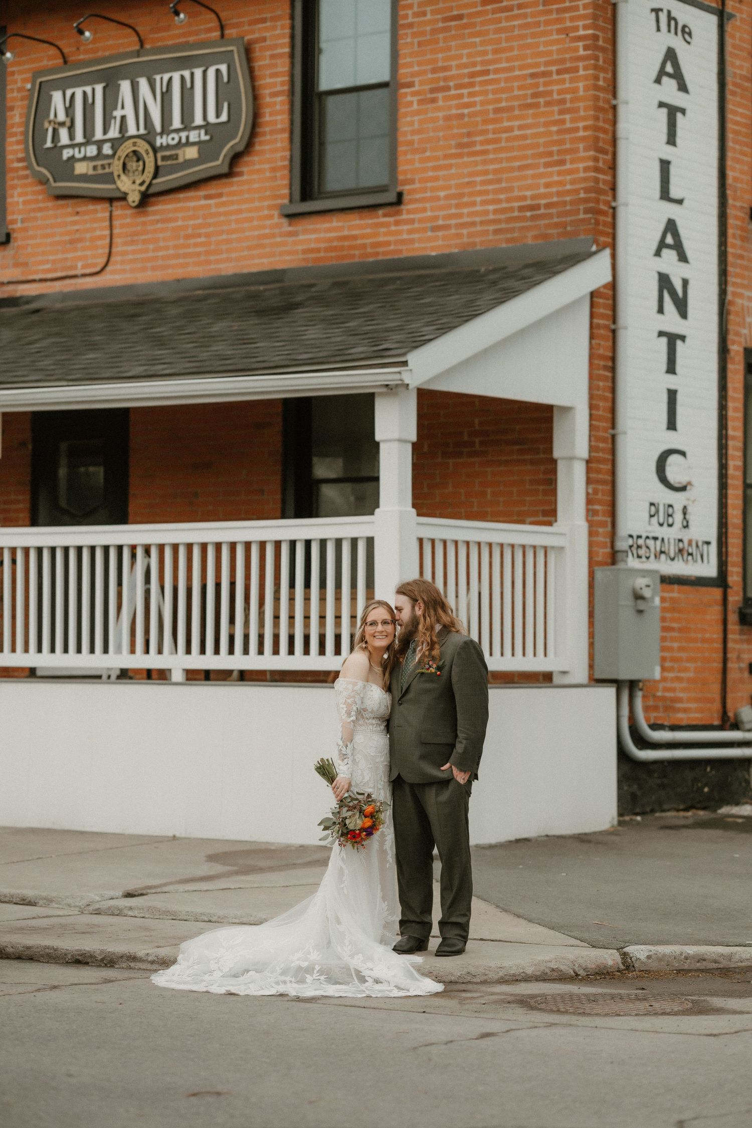 Couple poses outside The Atlantic building entrance with brick walls and white columns on their wedding day.