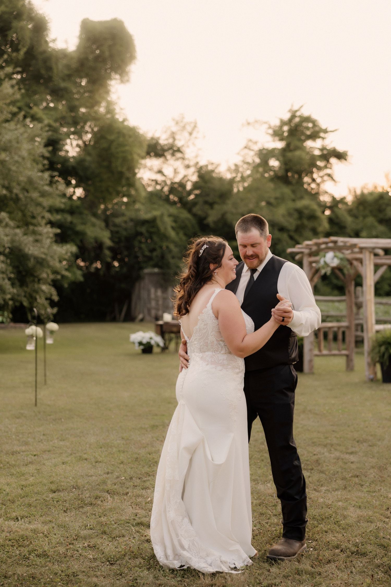 A couple shares a romantic dance moment at sunset in a garden with a wooden arbor.