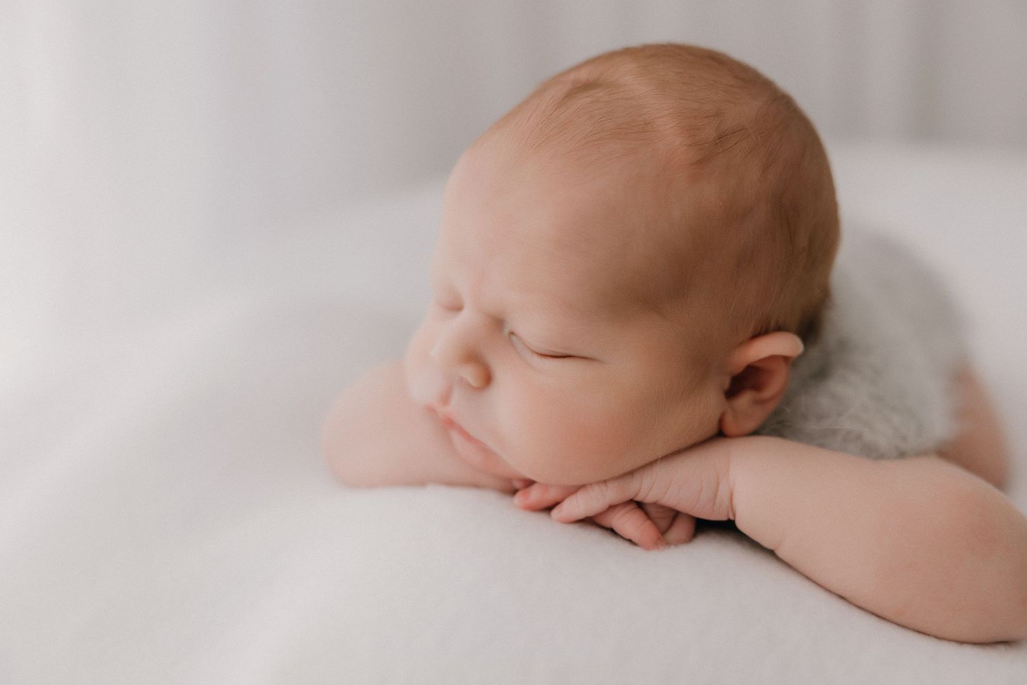 Sleeping newborn baby posed on white blanket in studio setting.