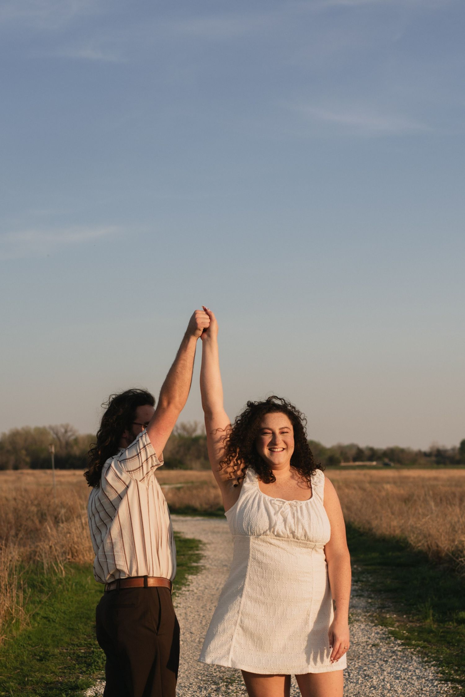 Two people hold hands raised in celebration on a gravel path at sunset.