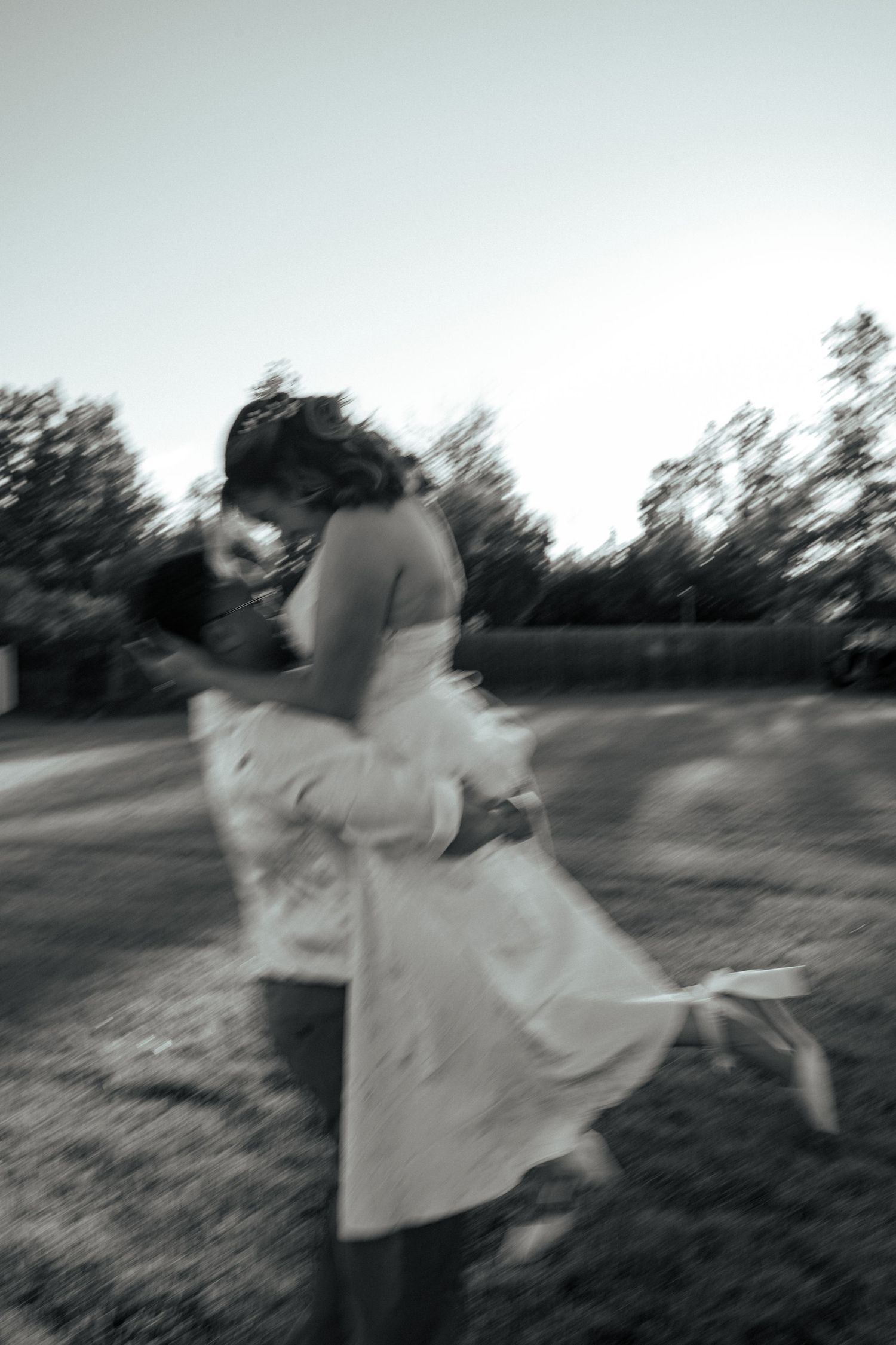 Black and white photo of a couple embracing and kissing outdoors in a park, captured with a romantic motion blur effect.