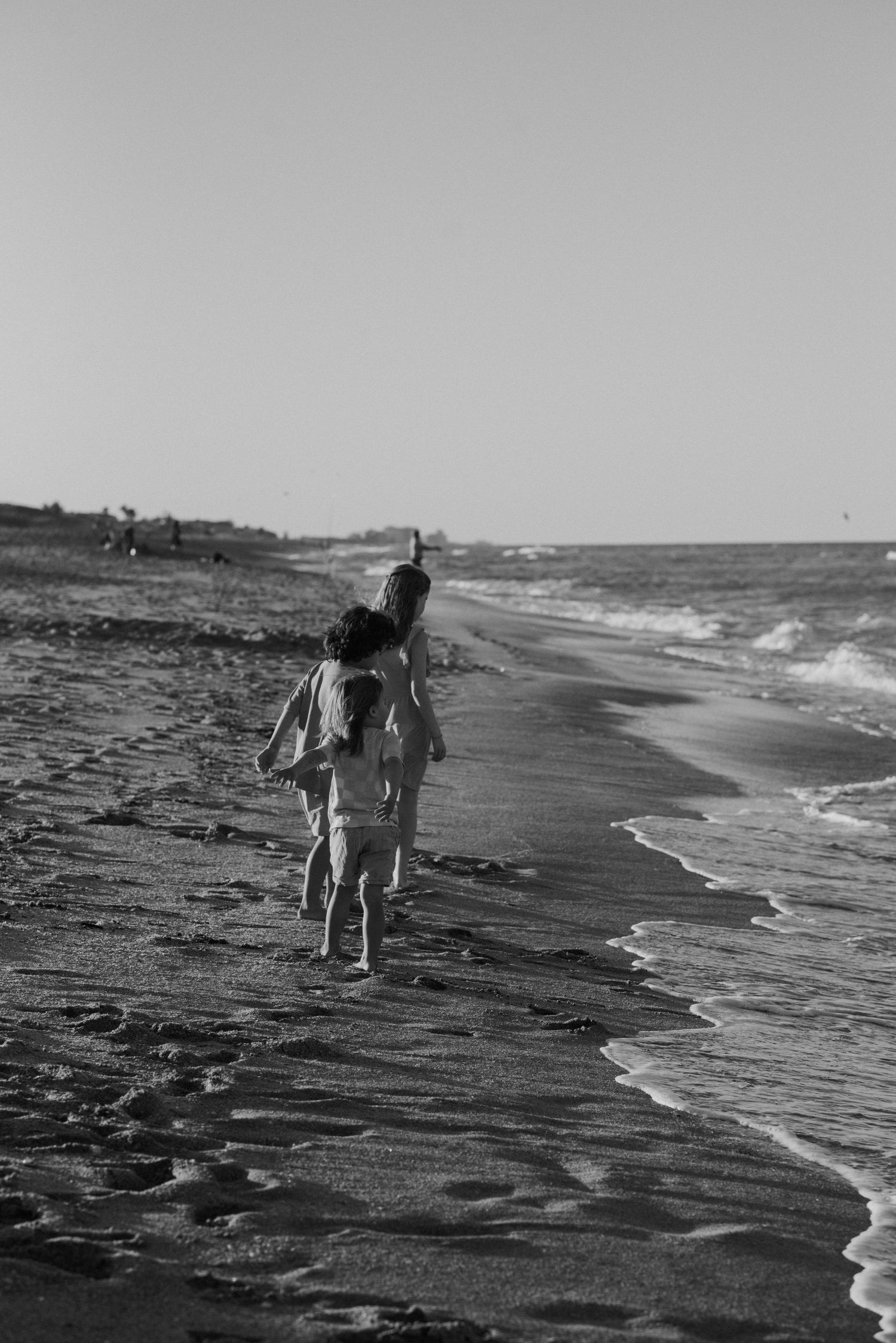 A figure walks along a misty beach shoreline in black and white, with waves lapping at the sand.