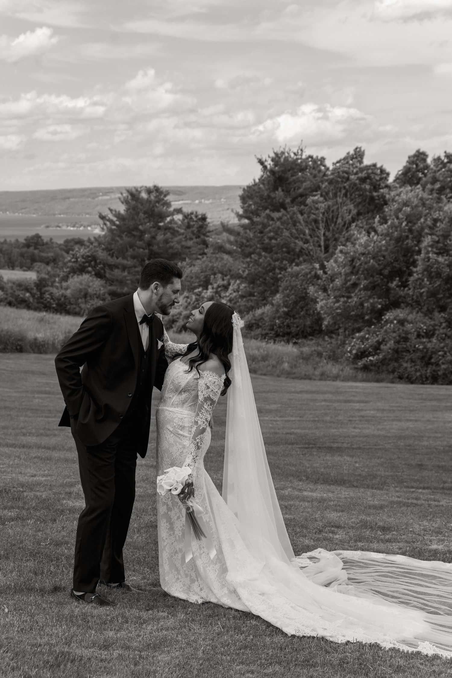 Black and white photo of a bride and groom sharing a romantic moment on a lush green lawn with scenic countryside views.
