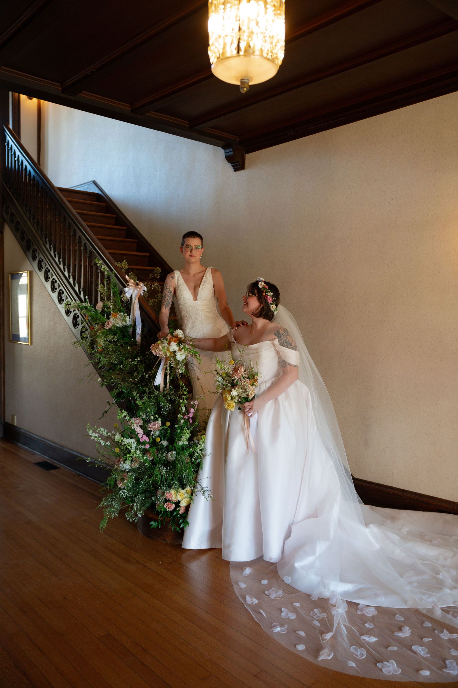 A wedding dress with a flowing train and floral arrangements decorates an elegant indoor venue with hardwood floors and lighting.