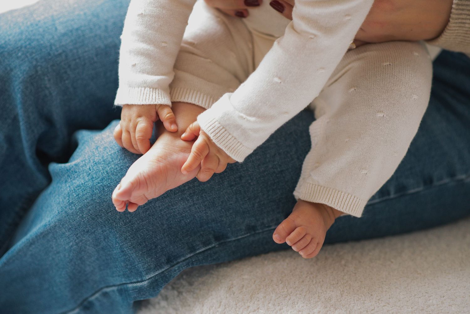Small bare feet of an infant wearing white clothing resting on a blue textured surface.