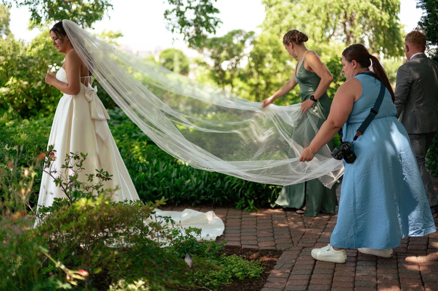 Wedding party holding and arranging a long flowing bridal veil in a garden setting.