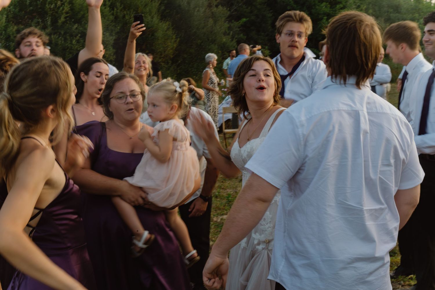 Guests dancing and celebrating outdoors at a wedding reception, wearing formal attire including purple bridesmaid dresses.