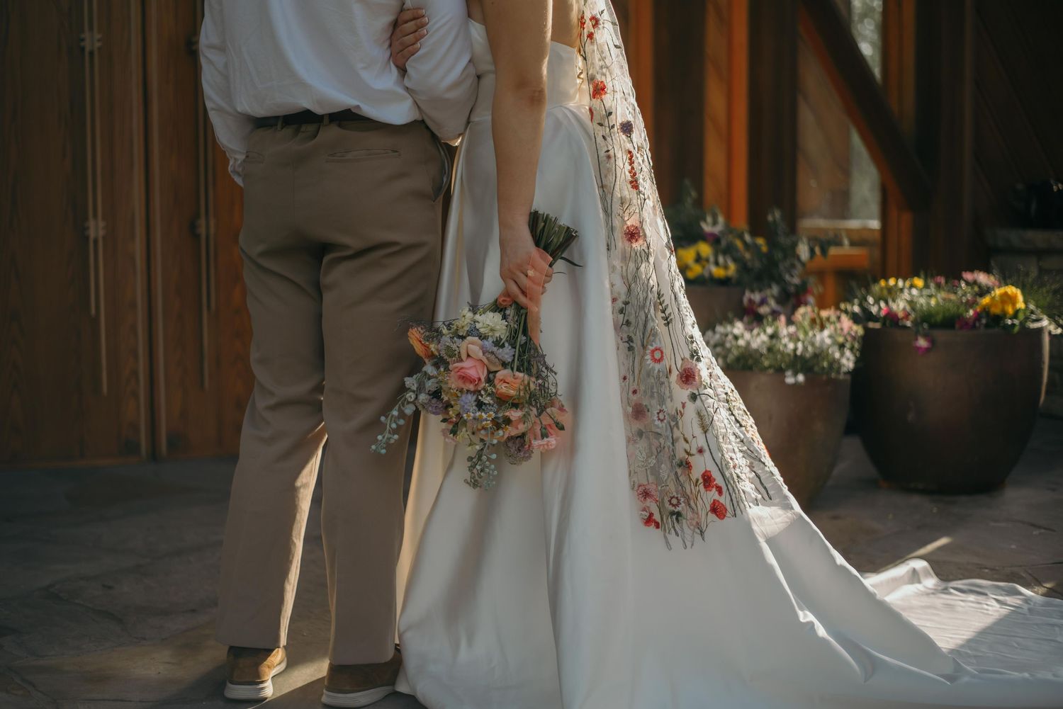 Bride and groom hold hands during outdoor wedding ceremony with rustic wooden backdrop and floral decorations.
