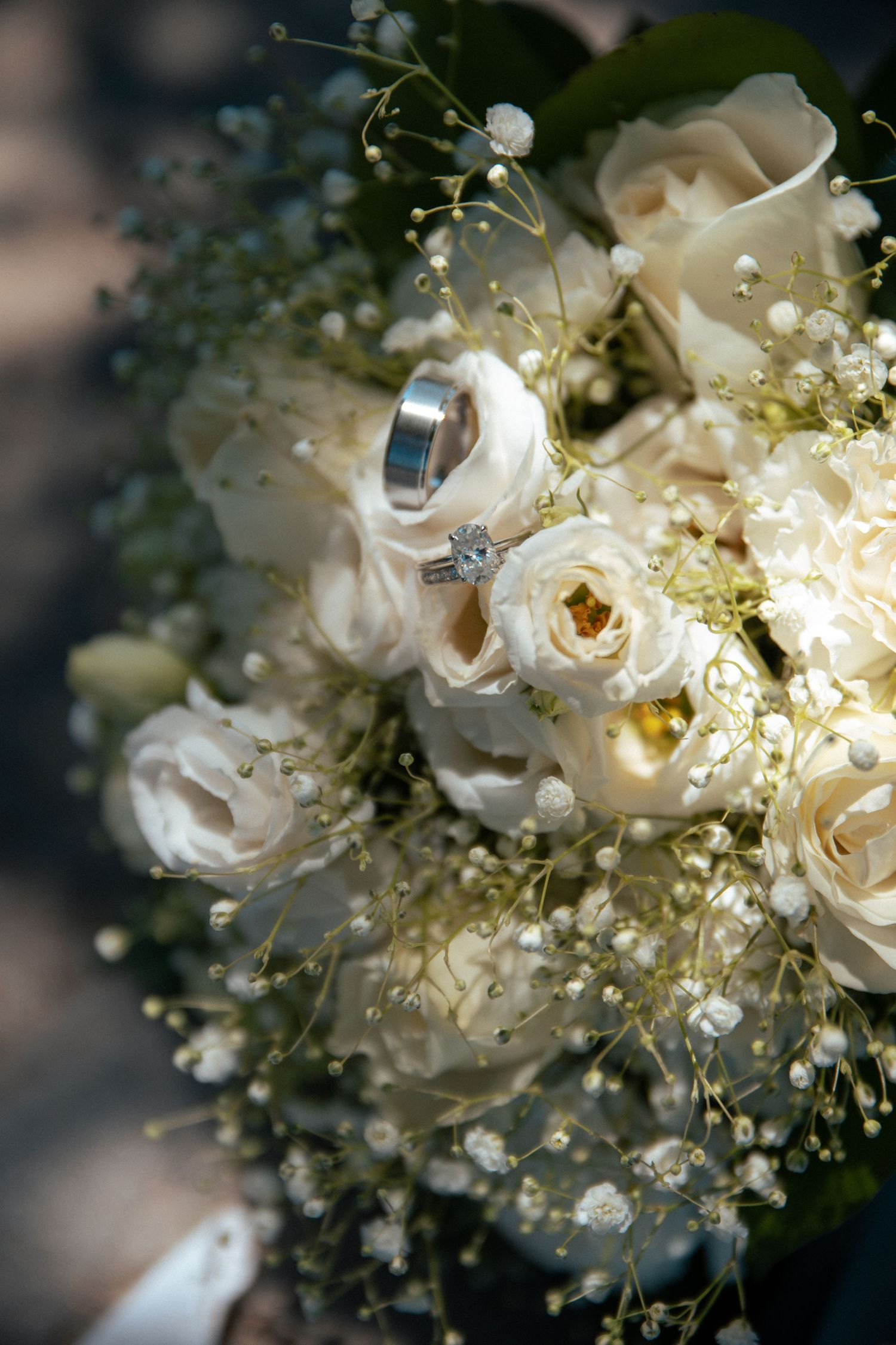 A wedding ring nestled among white roses and baby's breath in a bridal bouquet.
