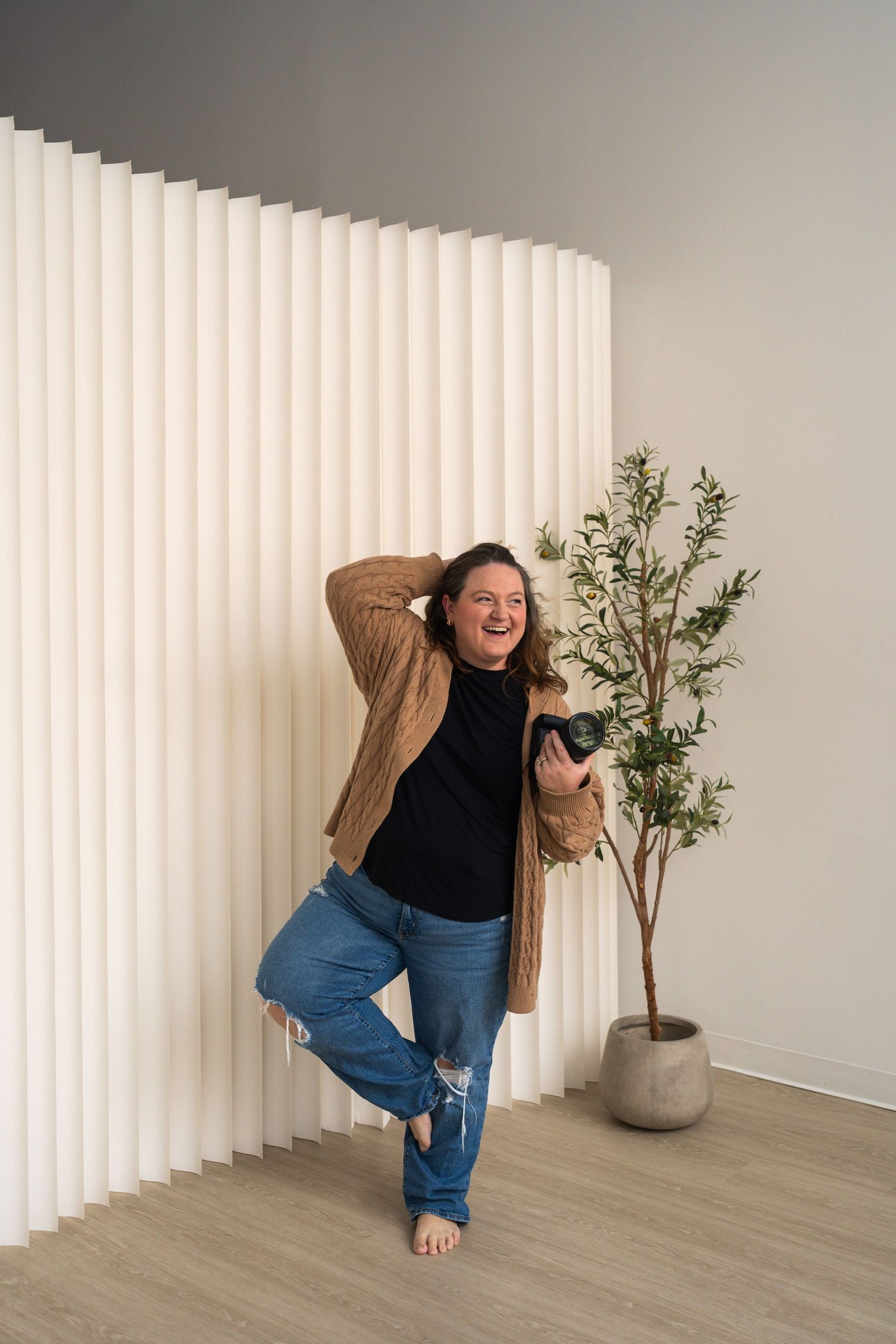 A series of four photos showing a figure in a black top and jeans playfully posing against a white wall with vertical blinds.