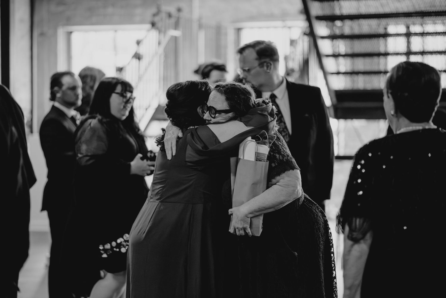 Black and white photo of wedding guests mingling and dancing at an elegant indoor reception.
