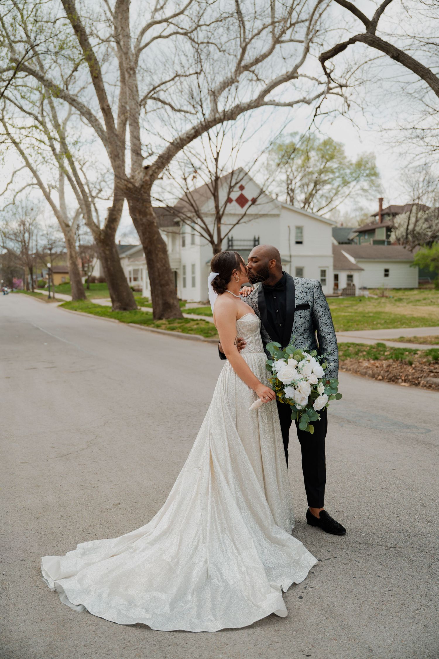 A couple sharing a romantic moment on a tree-lined street during their wedding day.