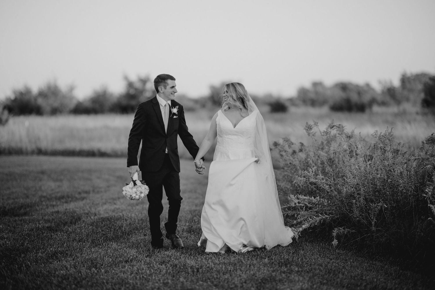 A couple walking through a field during their black and white wedding photoshoot.