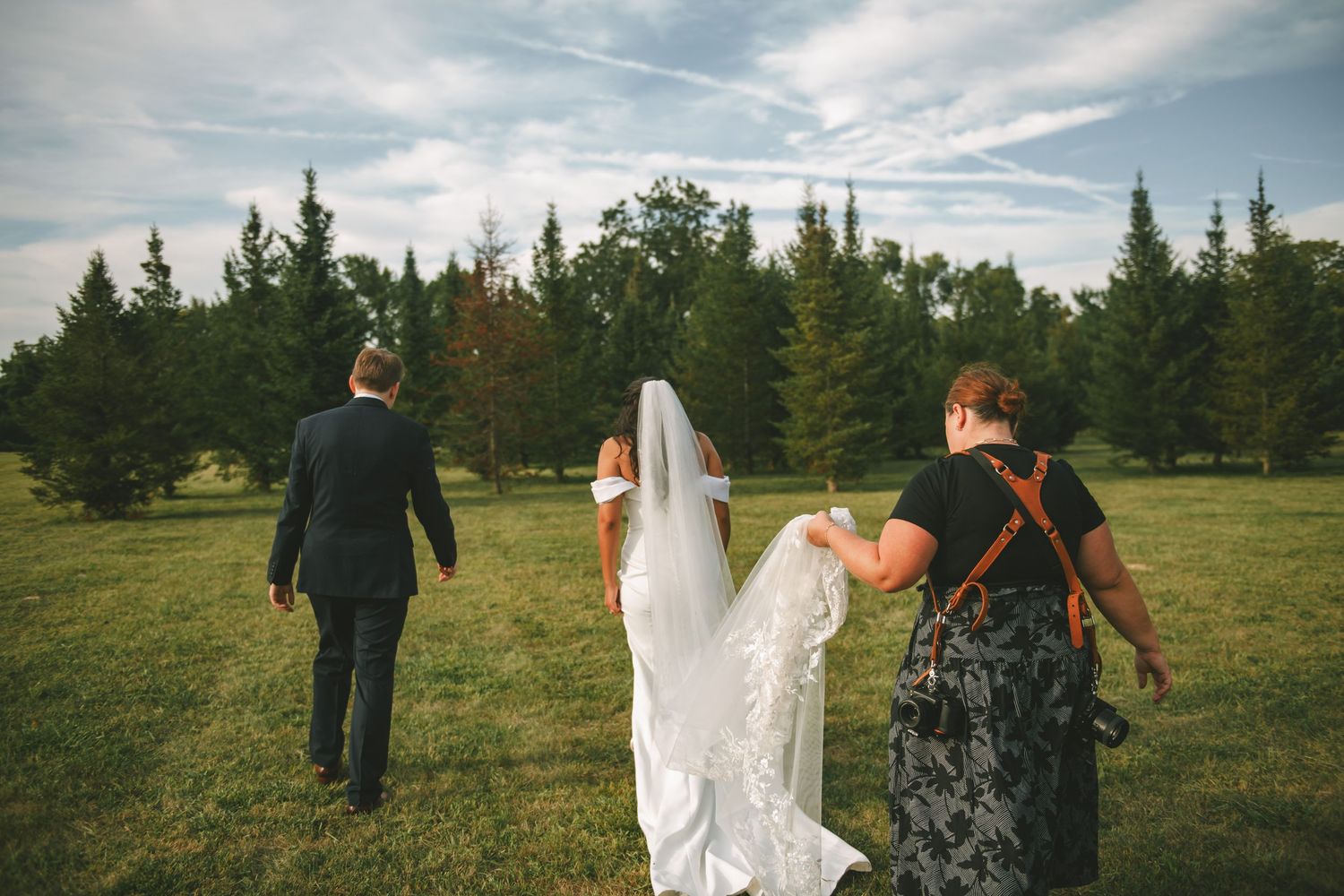 Wedding party walking through a sunny field with flowing dresses and formal attire.