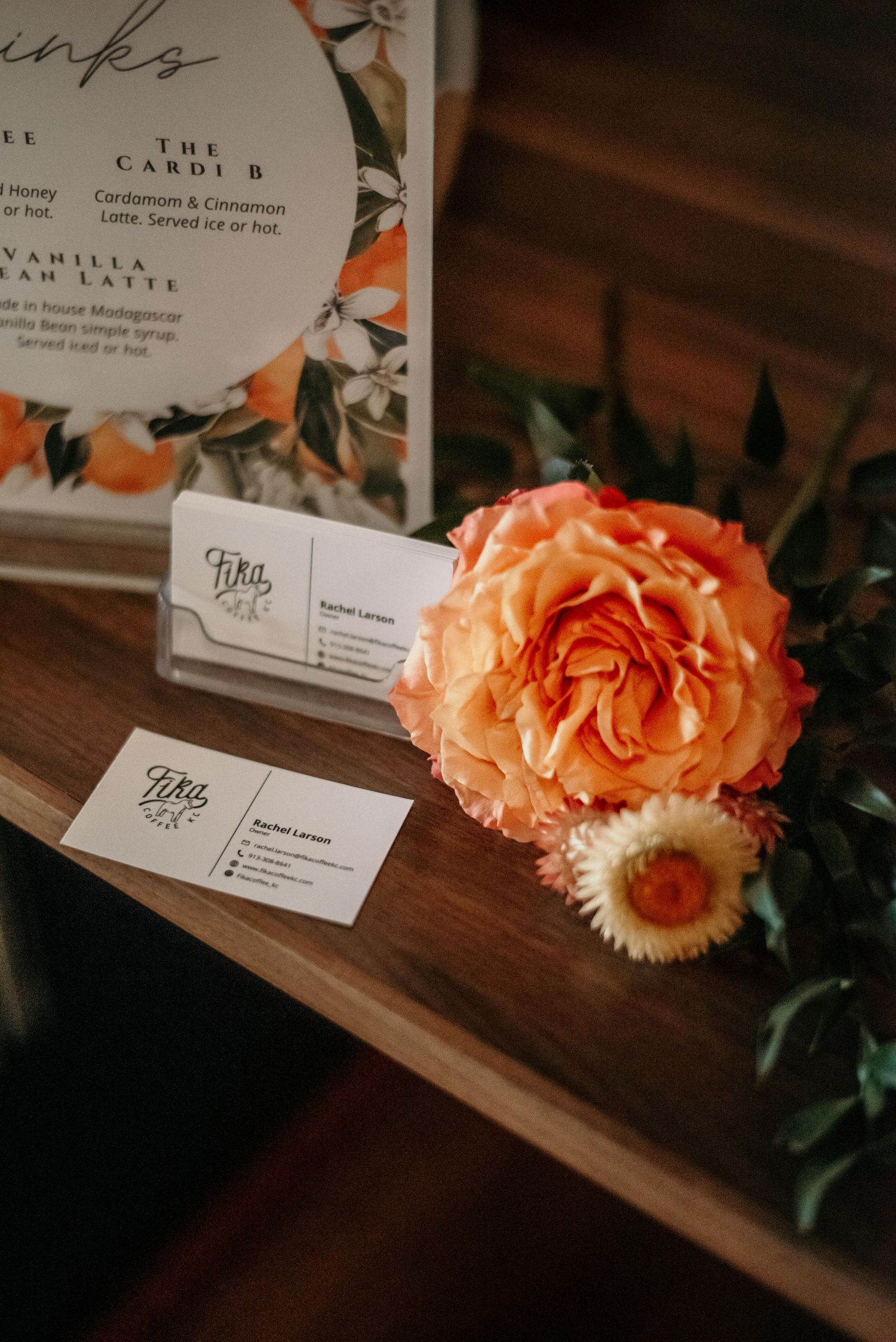 Business cards and orange peony flower displayed on wooden surface with floral menu card in background.