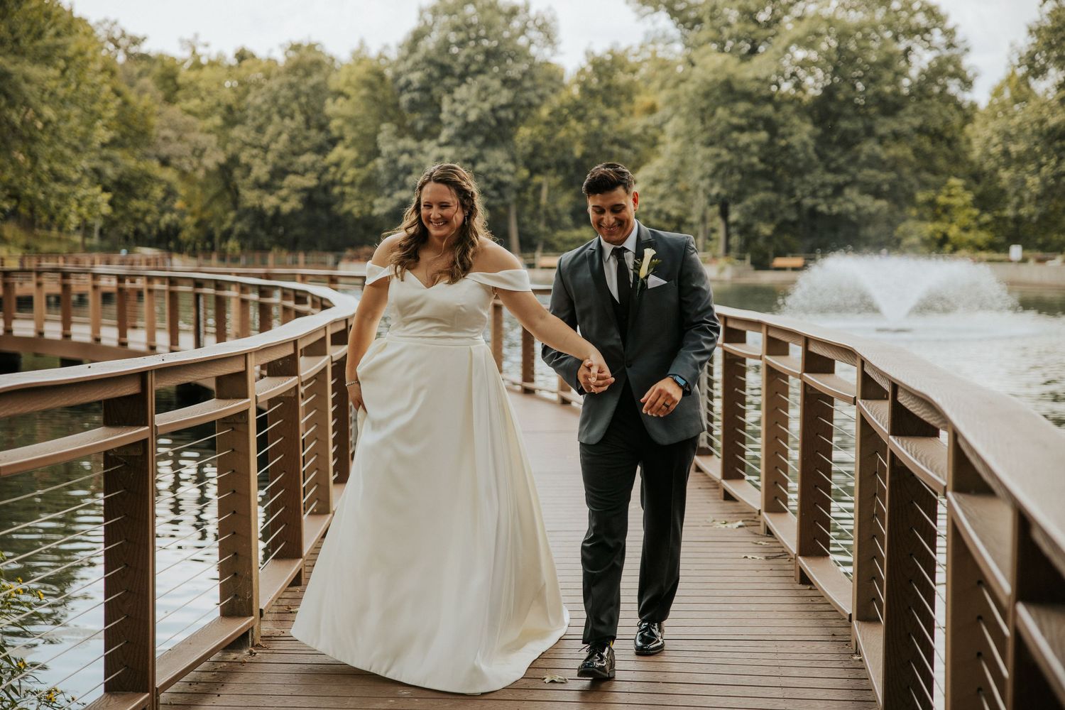 Wedding couple walking along a wooden boardwalk surrounded by nature and trees.
