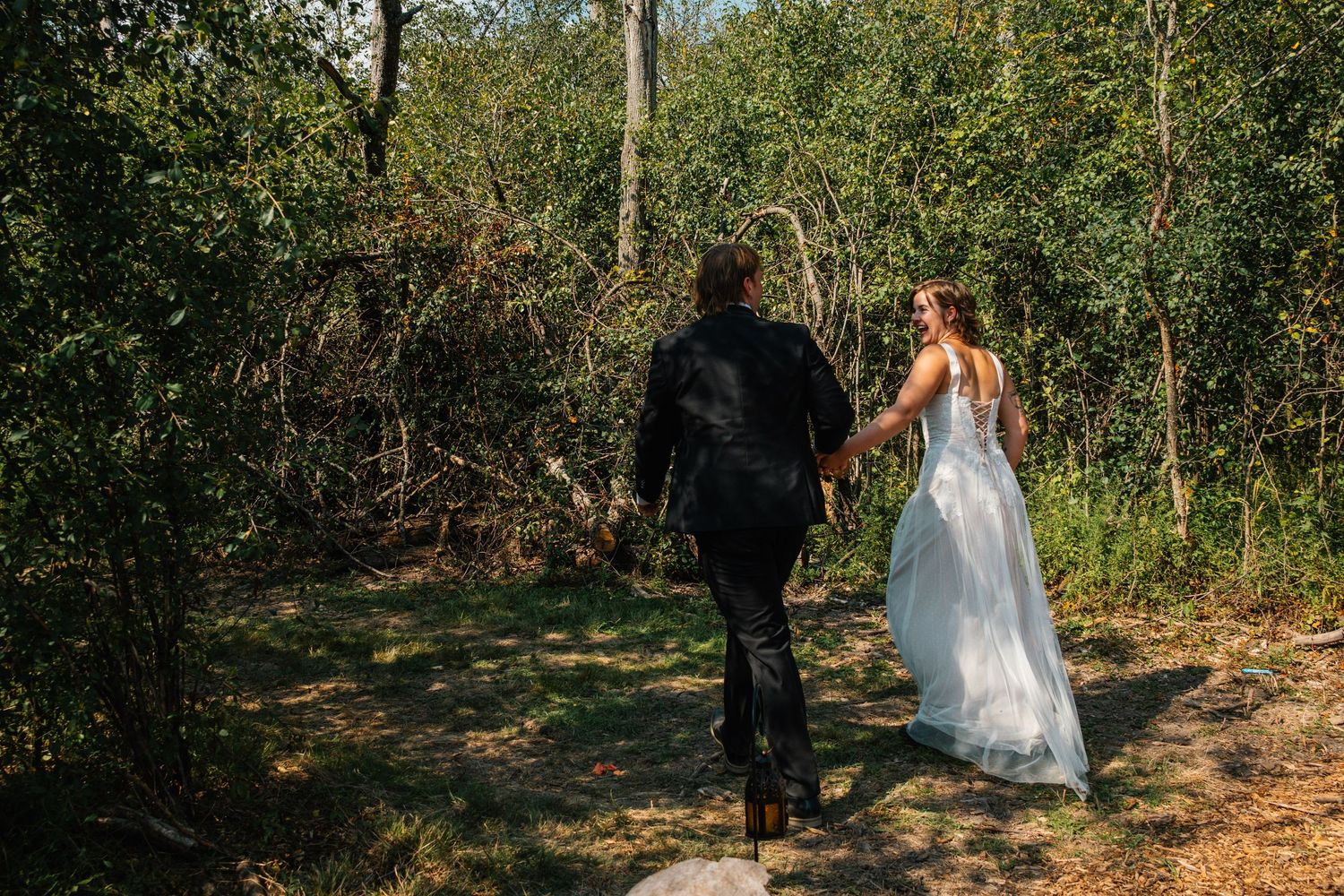 A bride and groom walk hand in hand through a lush forest path on their wedding day.