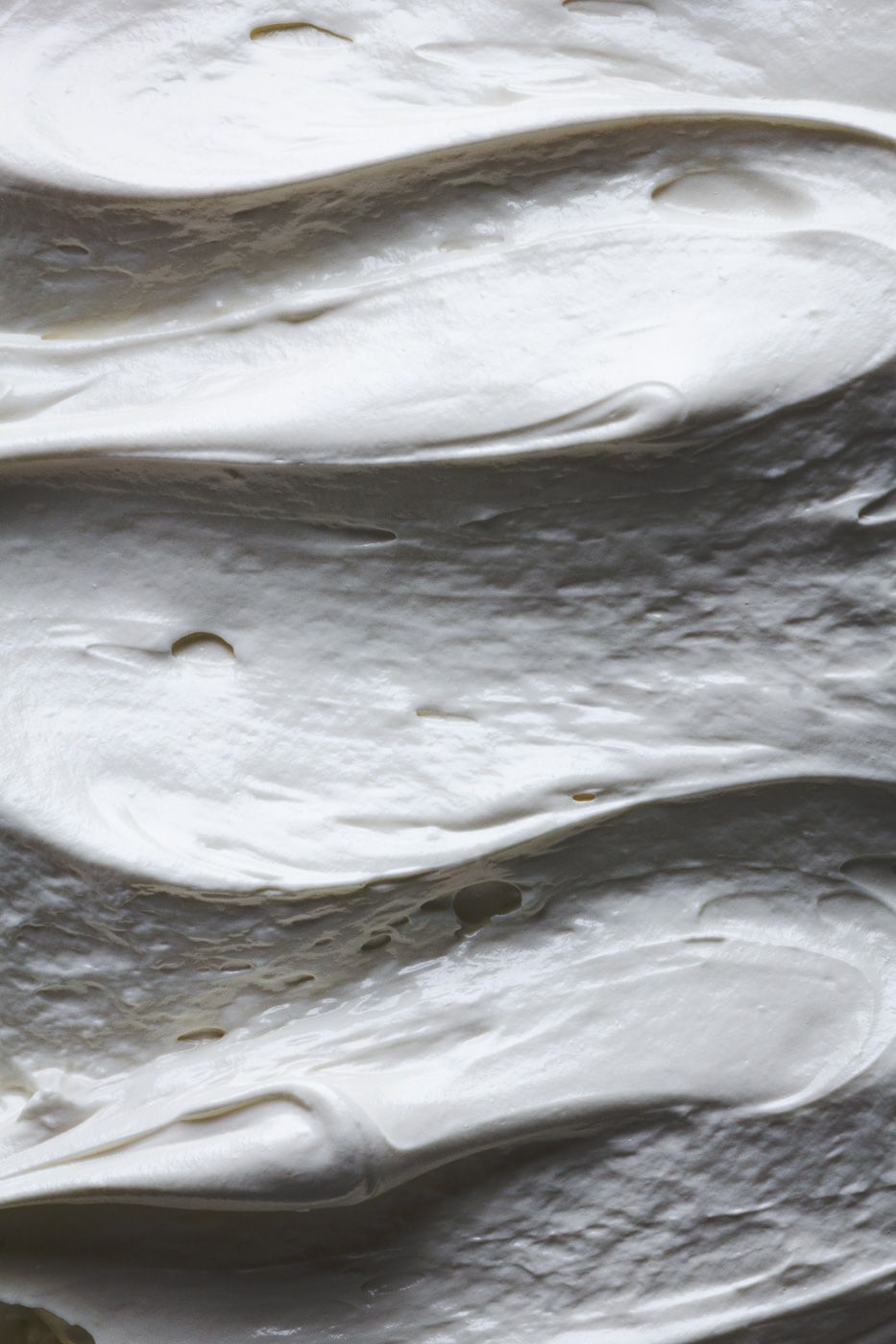 Close-up macro shot of smooth white frosting or meringue with soft wavy rippled texture and shadows.