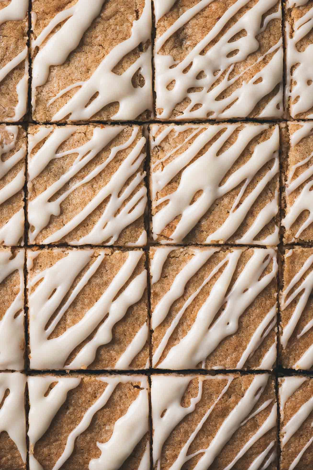 Freshly baked blondies cut into squares and drizzled with white icing in a diagonal pattern.