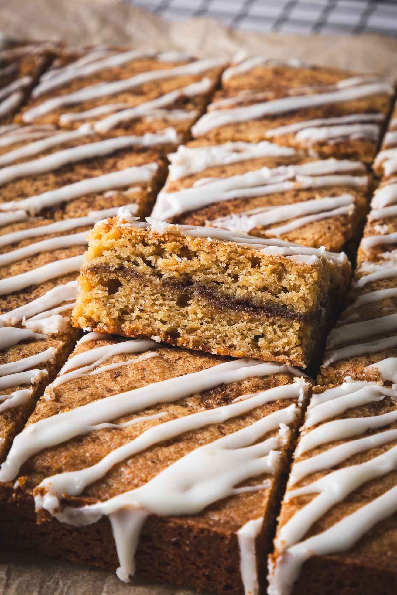 Freshly baked cookie bars with chocolate chips drizzled with white icing in a diagonal pattern on parchment paper.