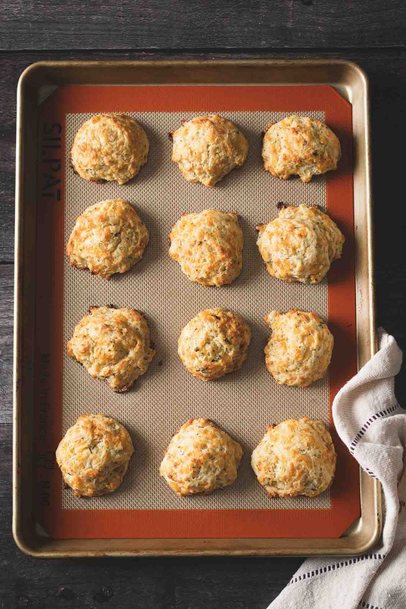Freshly baked savory cheese biscuits arranged on a baking sheet lined with a silicone baking mat.