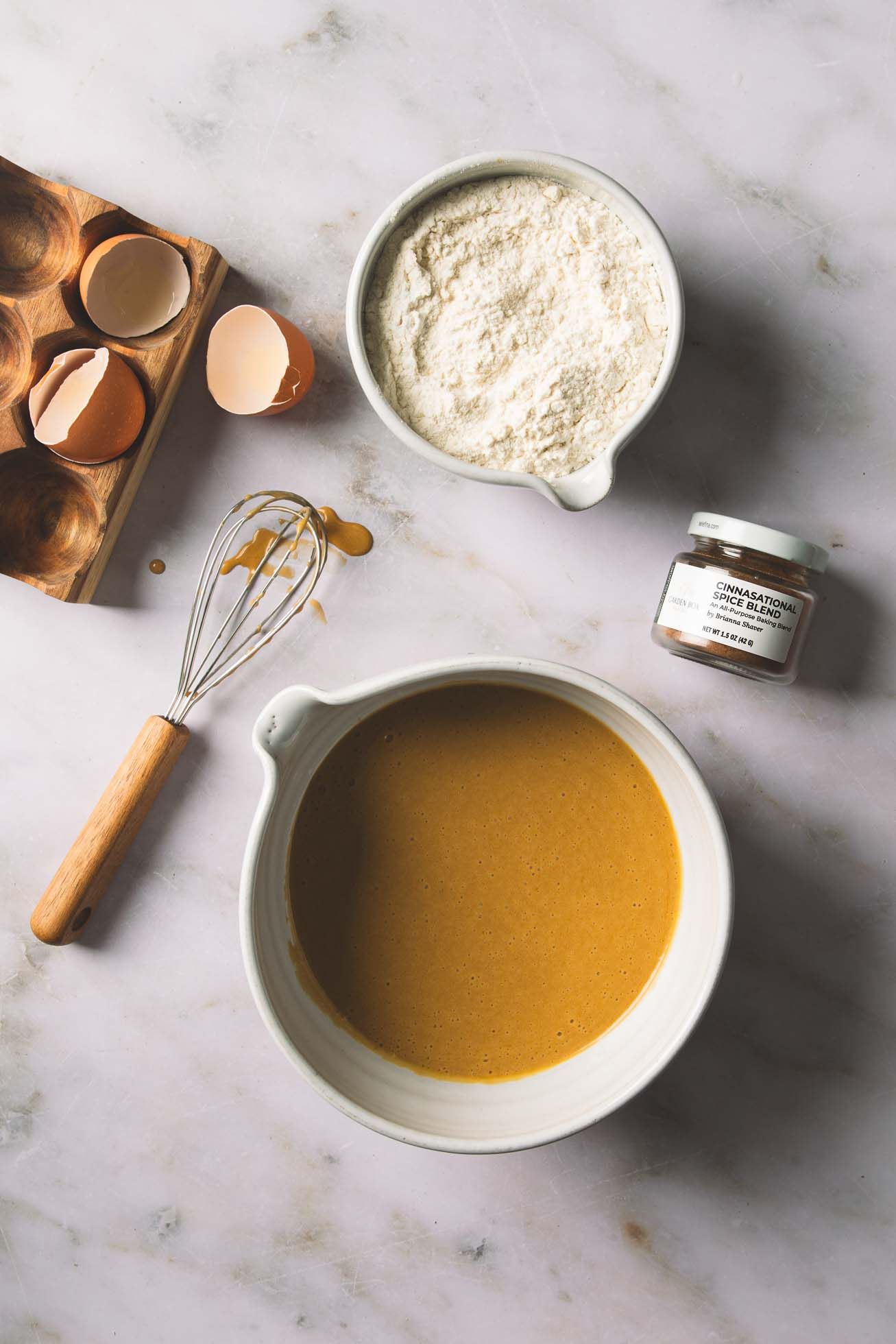 Golden caramel sauce pours into a white ceramic mixing bowl filled with flour and cracked eggshells on the side.