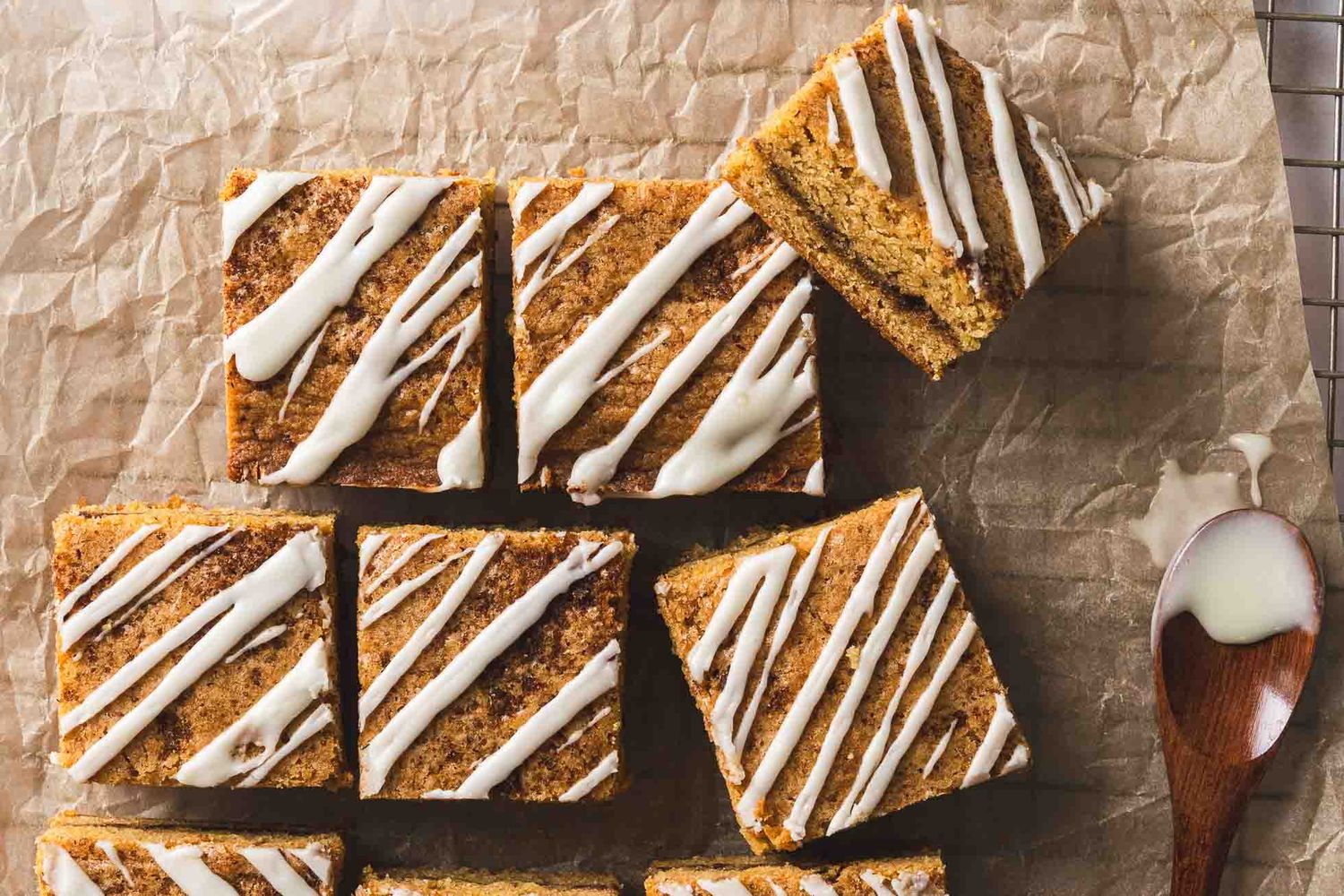 Square pumpkin spice bars with cream cheese drizzle arranged on brown parchment paper with a wooden spoon.