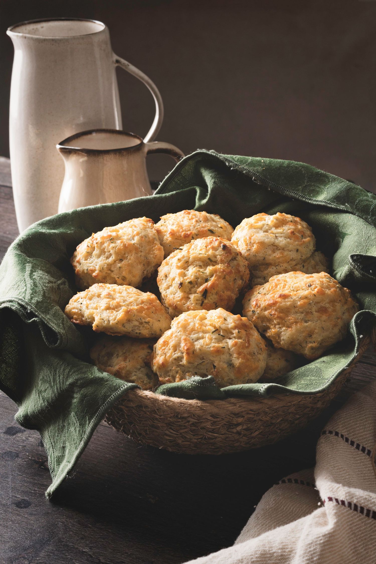 Freshly baked biscuits served in a rustic basket with green napkins and ceramic pitchers in the background.