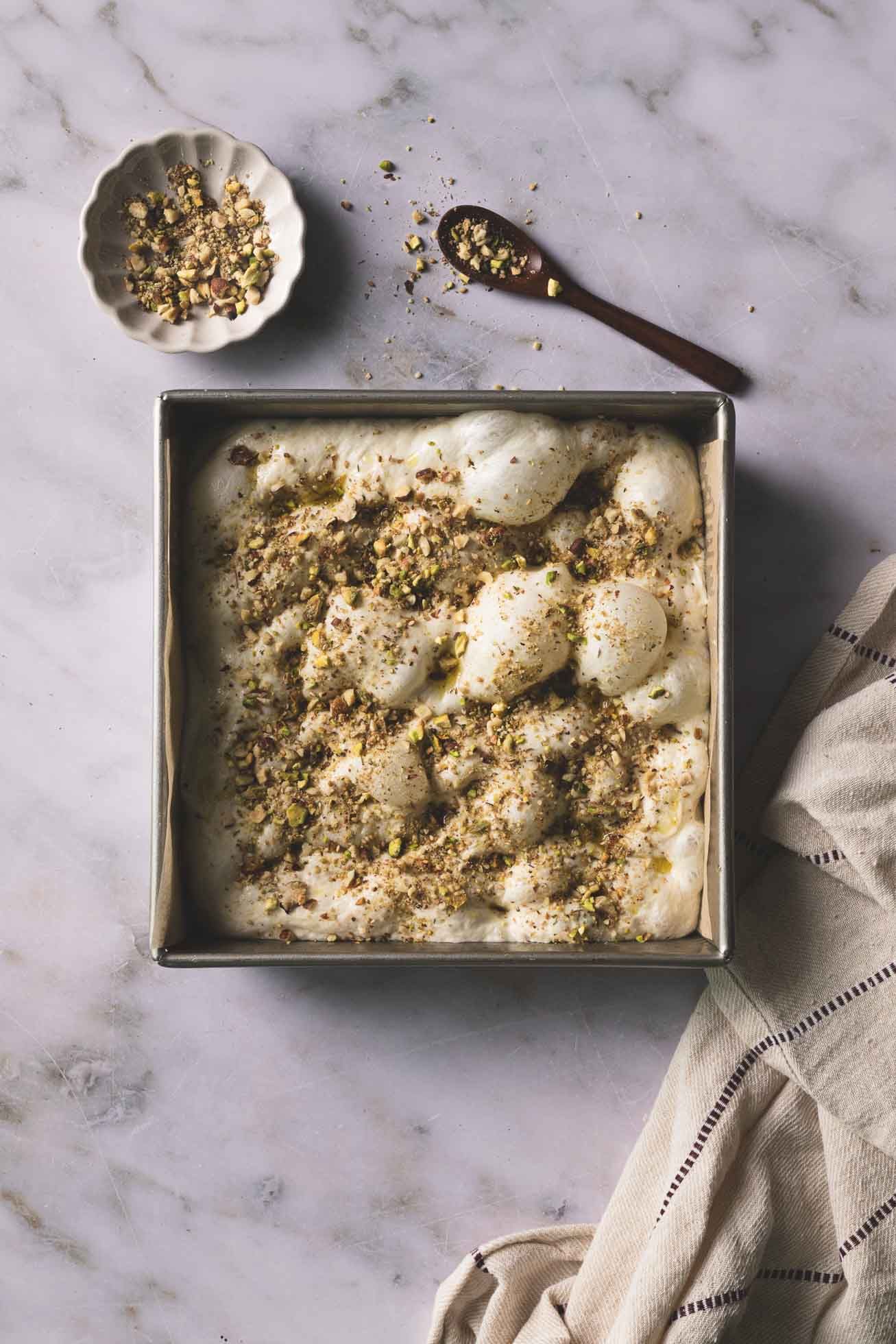 Ice cream with crumbled nuts topping served in a square baking pan on marble counter with linen napkin.