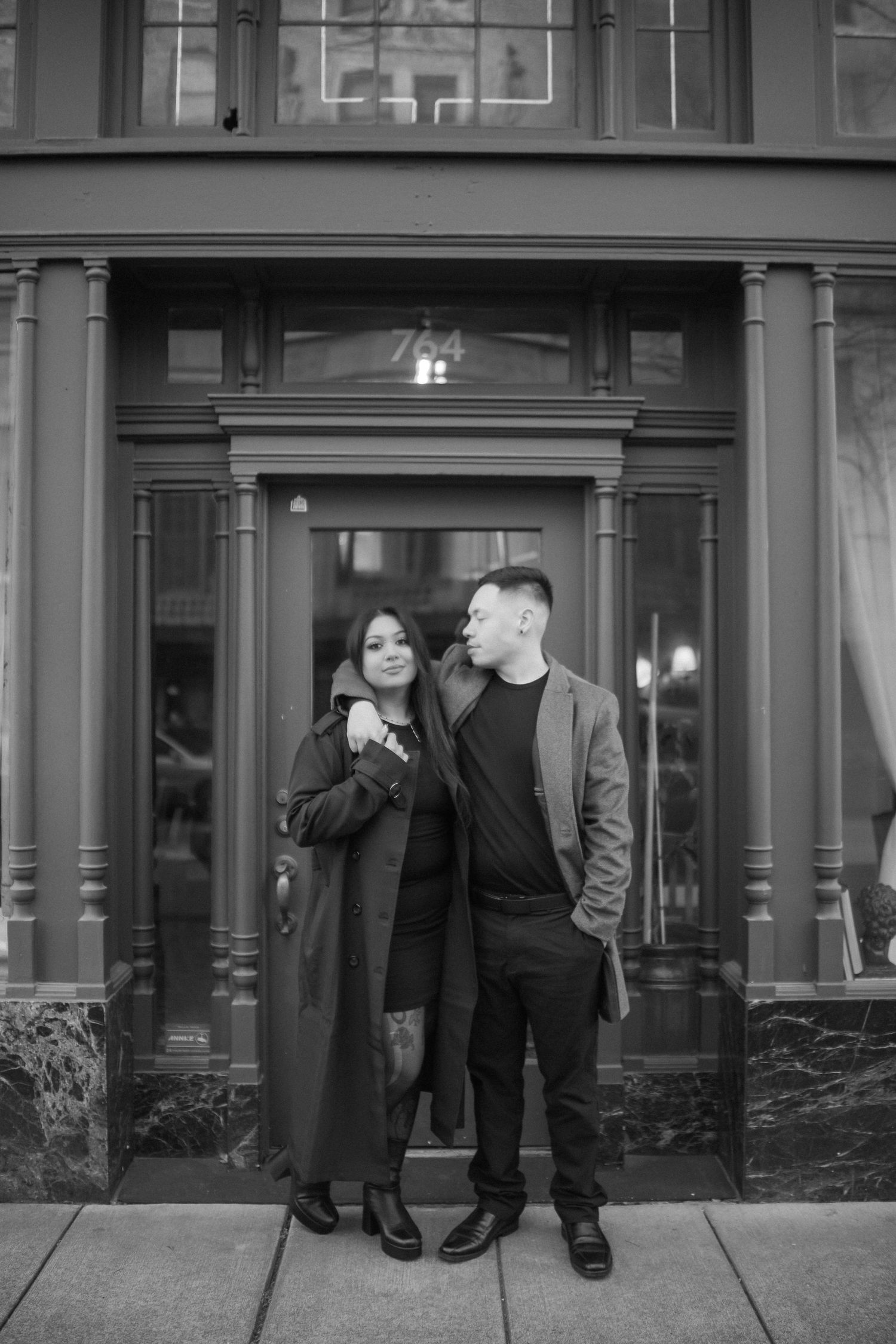 Black and white portrait of a couple standing together in front of a building entrance