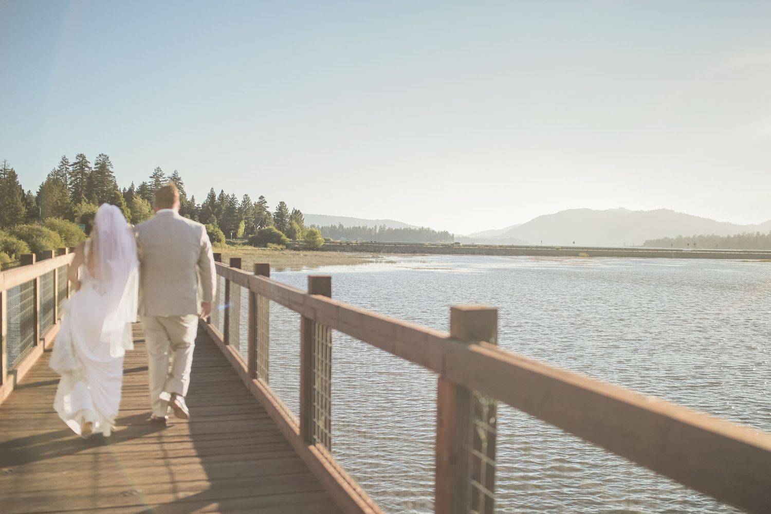 Bride and groom walking along a wooden dock by the lake during their wedding day