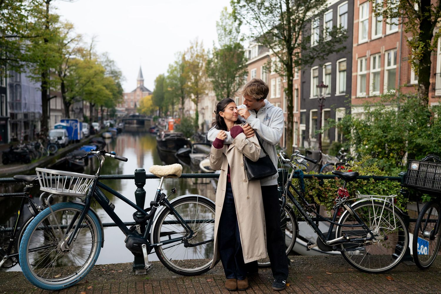 Couple sharing a warm moment on an Amsterdam canal bridge, surrounded by parked bicycles and autumn trees.