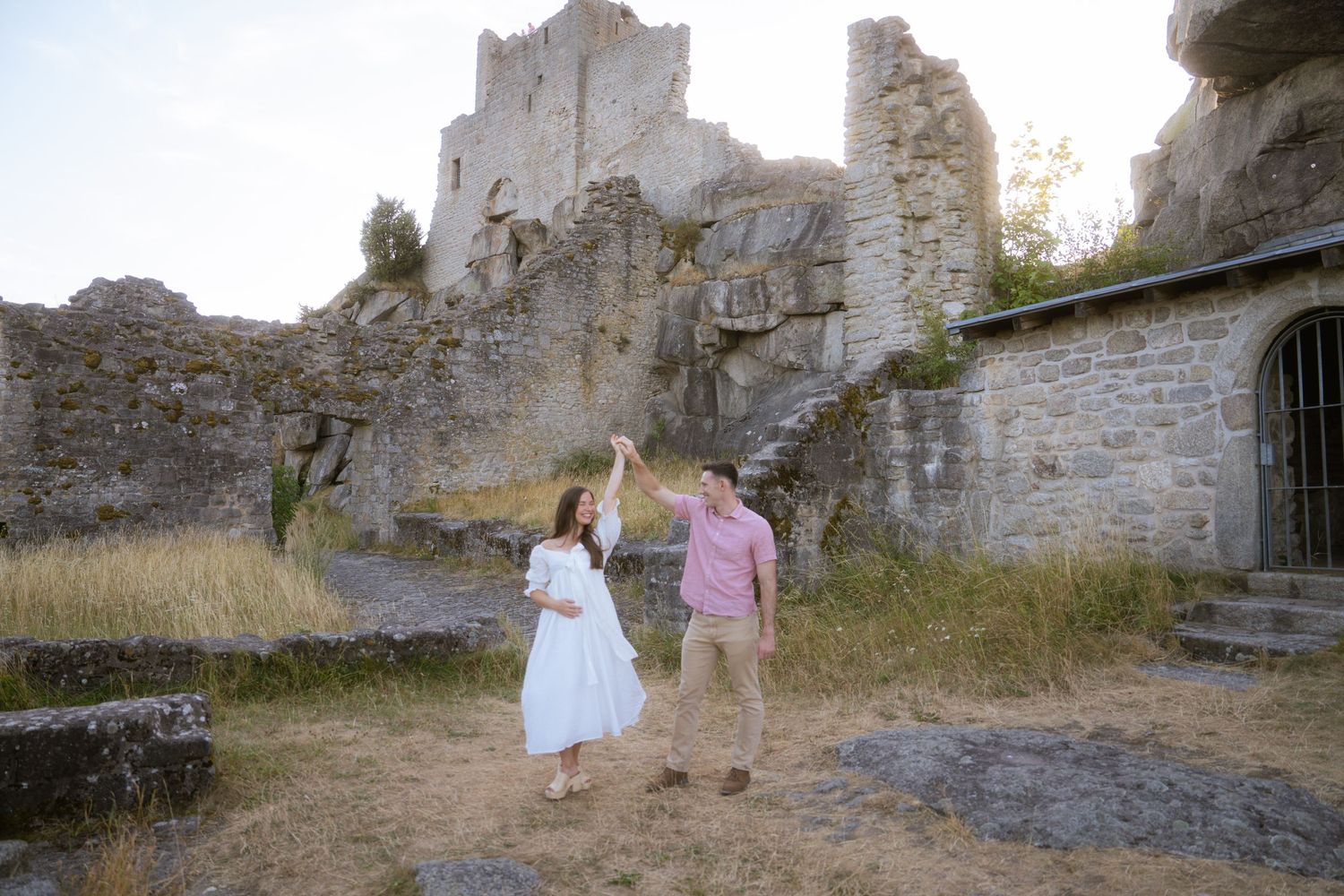 Couple dancing outdoors amid ancient stone castle ruins, the woman in a white dress twirling under her partner's raised arm.