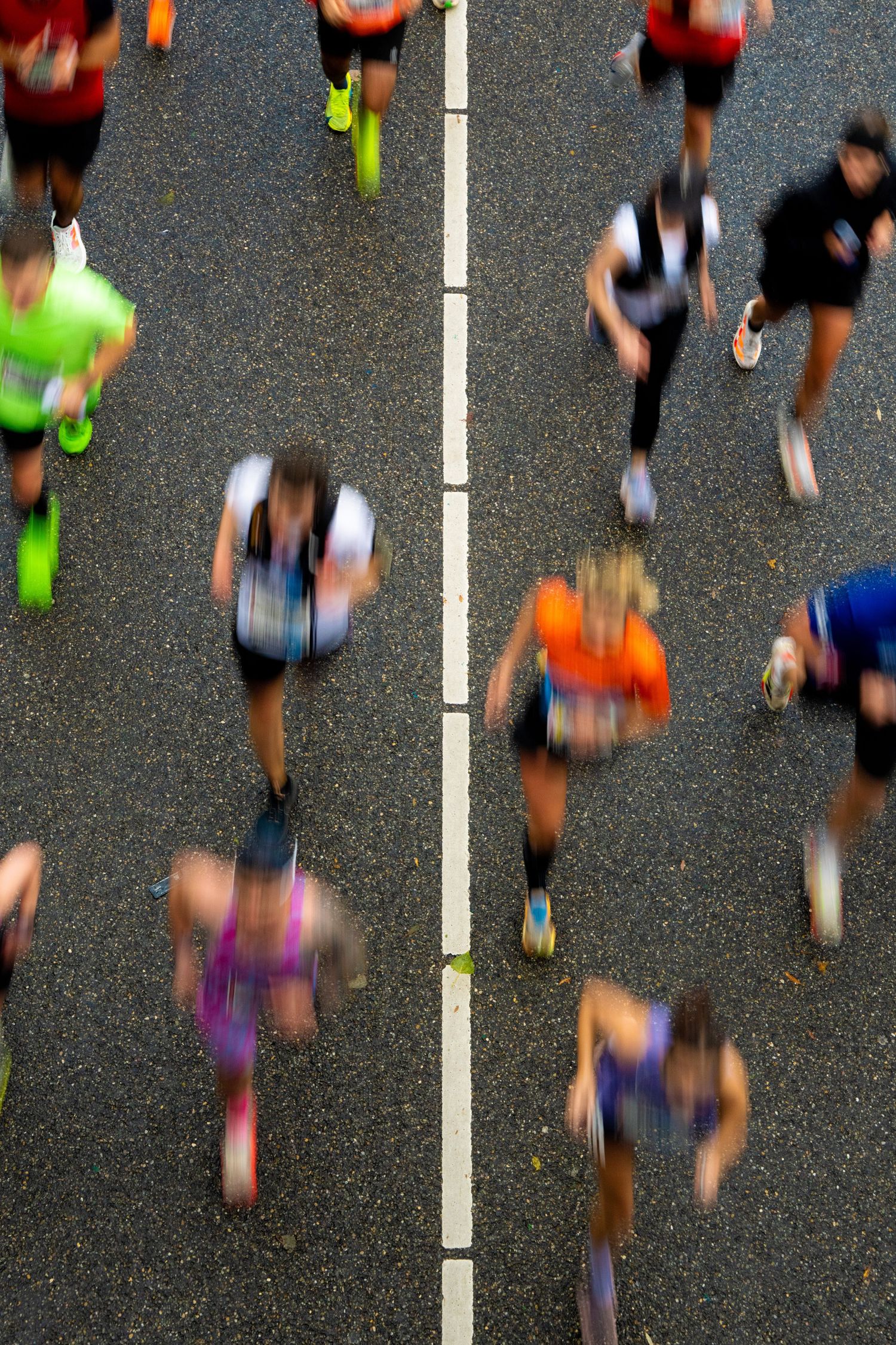 Overhead motion-blurred view of colorful marathon runners racing along a road divided by a white line.