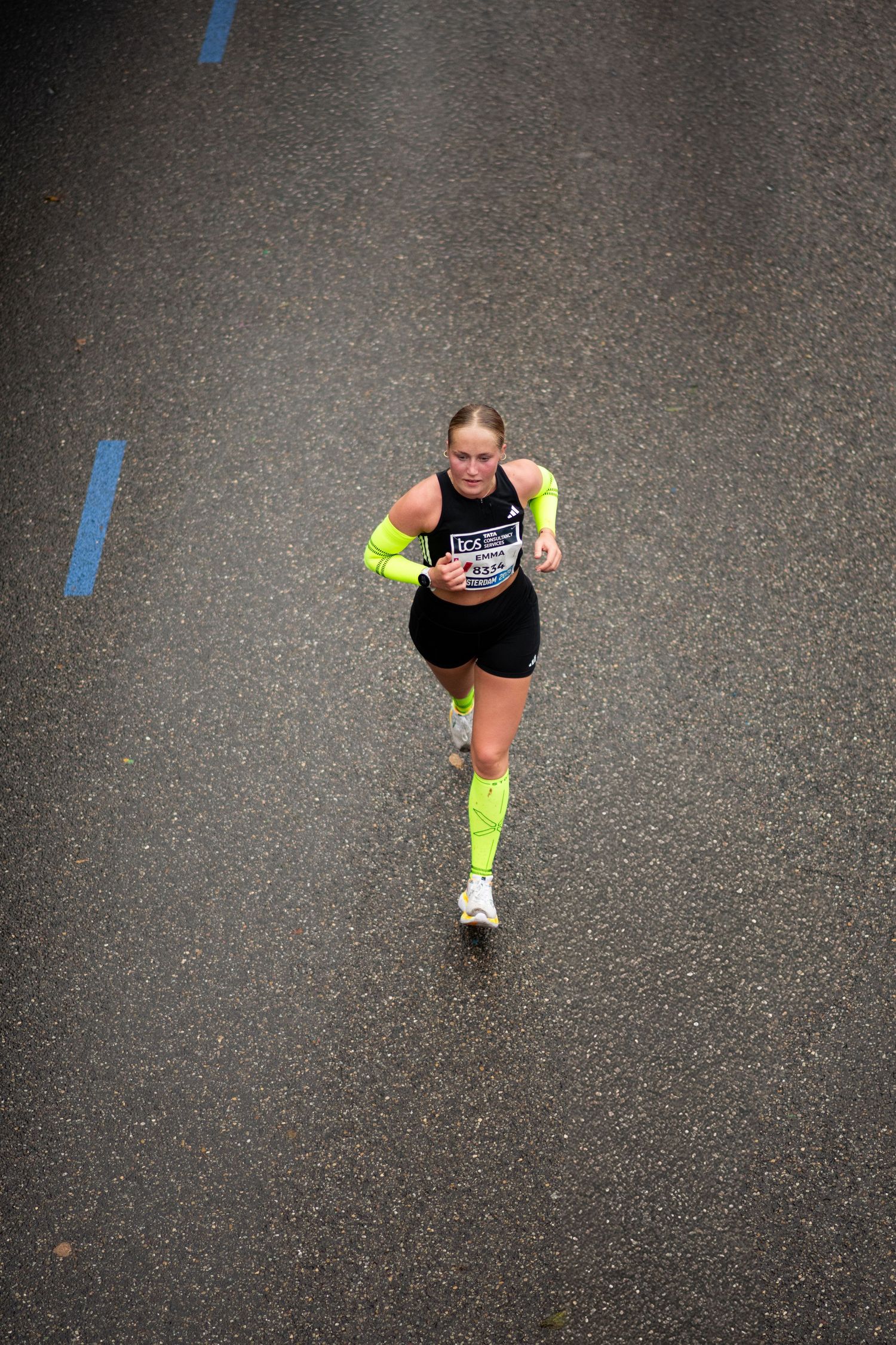 Aerial view of a female marathon runner in neon yellow sleeves and socks running on wet asphalt during a race.