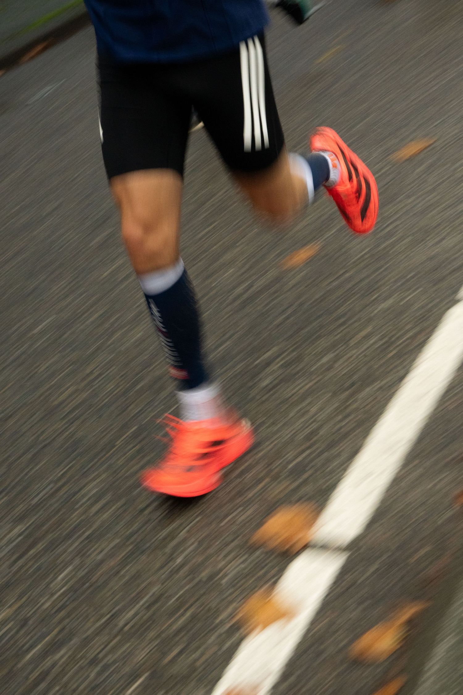 Motion-blurred runner in black shorts, navy compression socks and bright orange running shoes races along an asphalt road.
